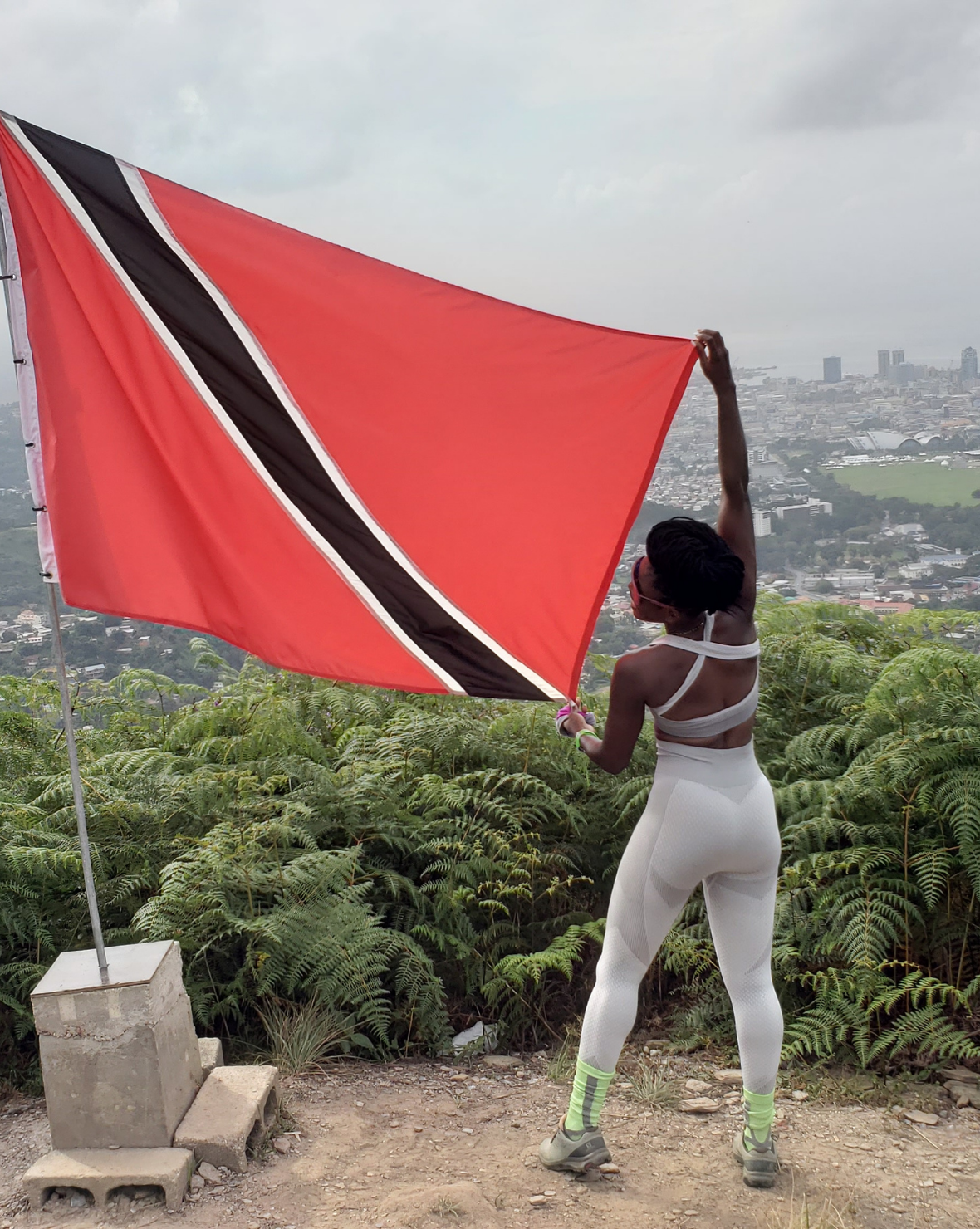 a woman holding a Trinidad and Tobago flag on top of a hill