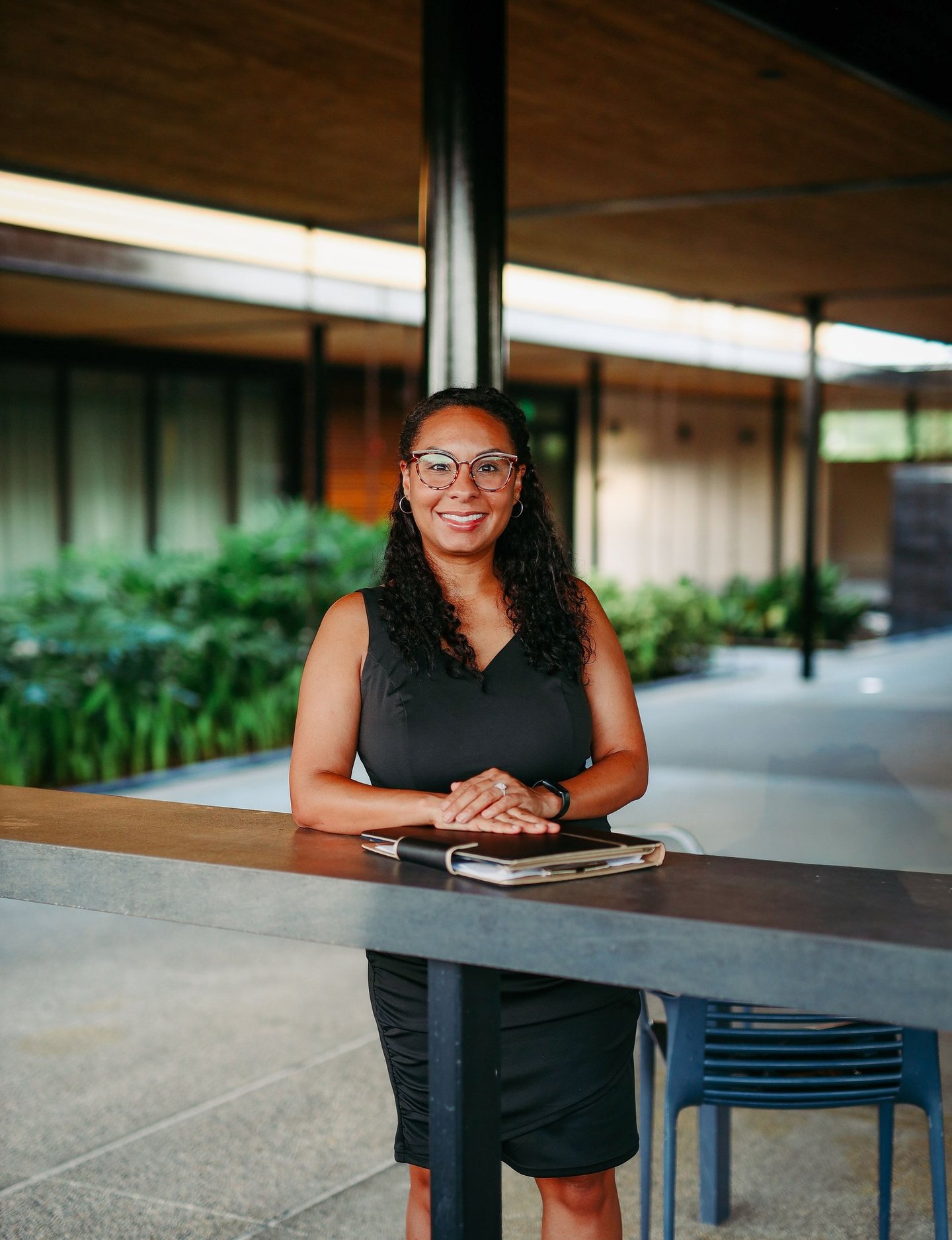 A smiling Lakeland wedding officiant in a black dress and glasses standing in a venue courtyard.