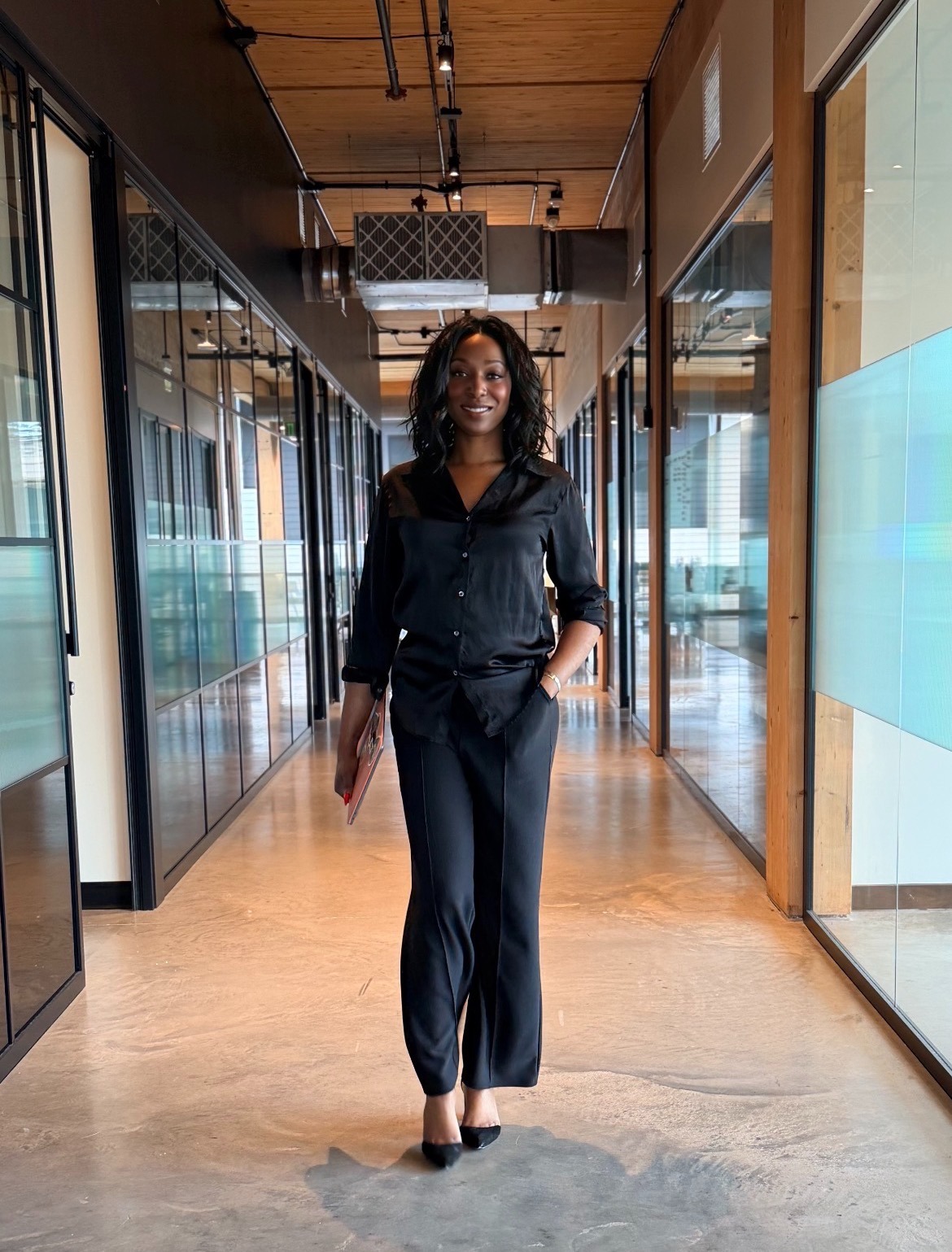 Ain in a black business suit walking through a modern glass-walled office hallway.