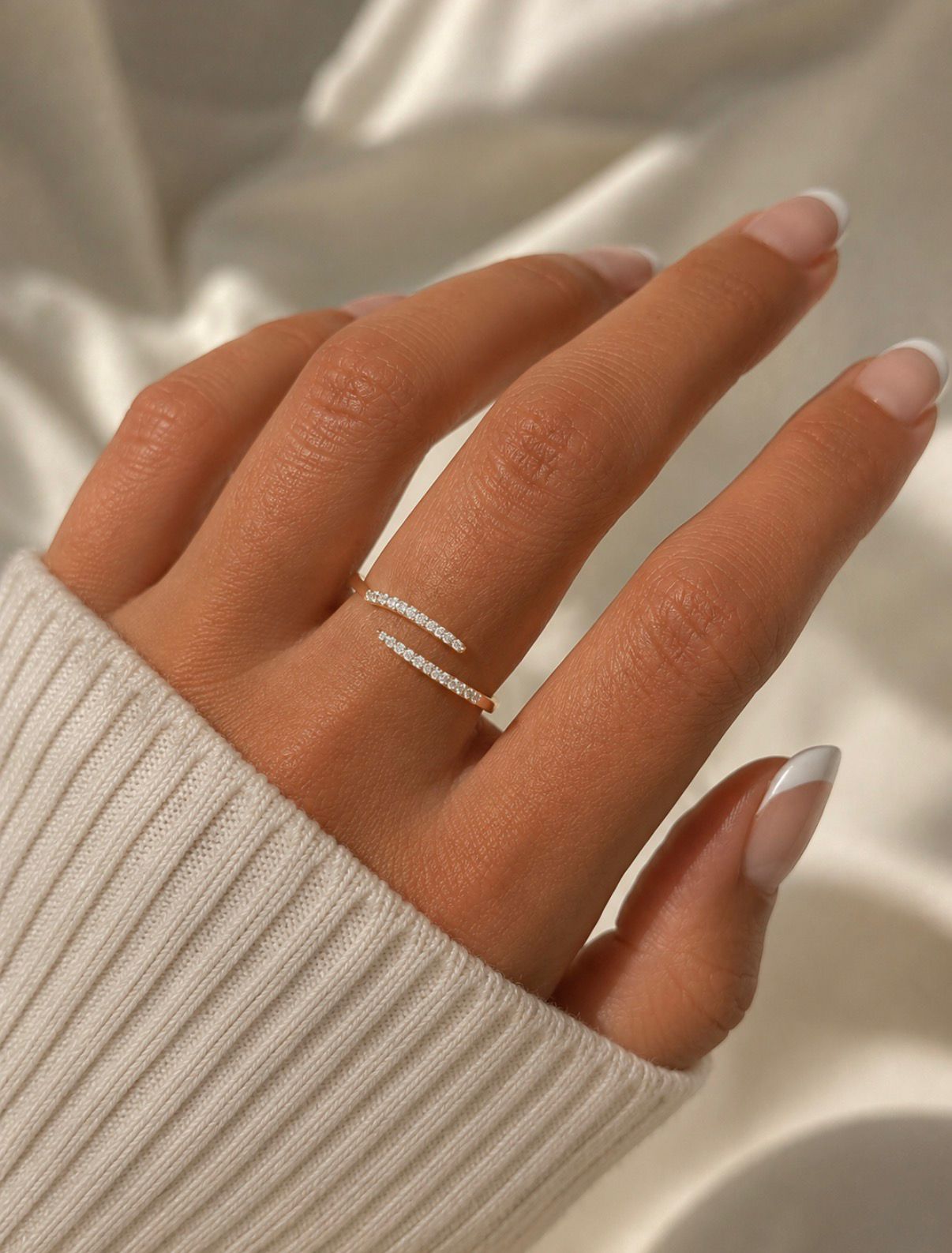 Close-up of a gold crystal open ring worn on a hand with a soft cream sweater sleeve.