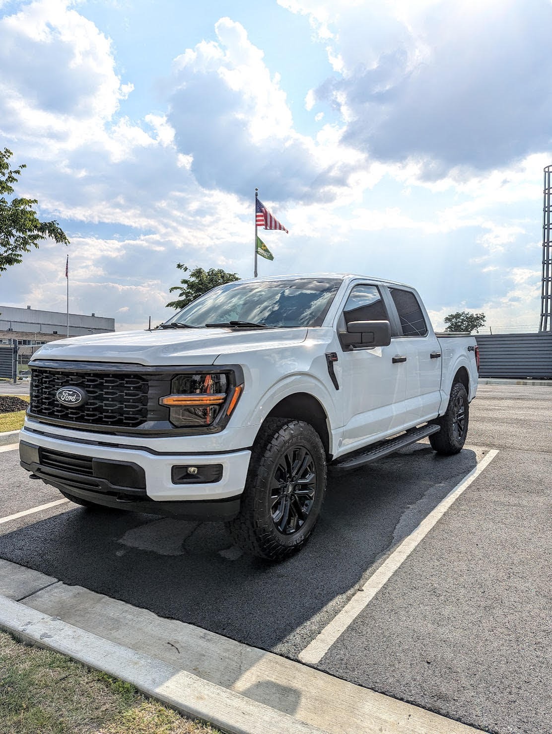 A white Ford F-150 Lariat pickup truck with black wheels parked in an asphalt lot under a cloudy sky.