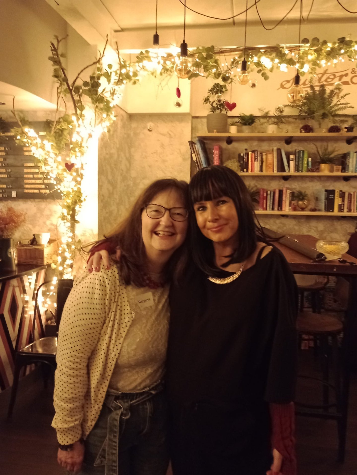 two woman have their arms around each other. They are smiling. They are at a Traitors themed party.