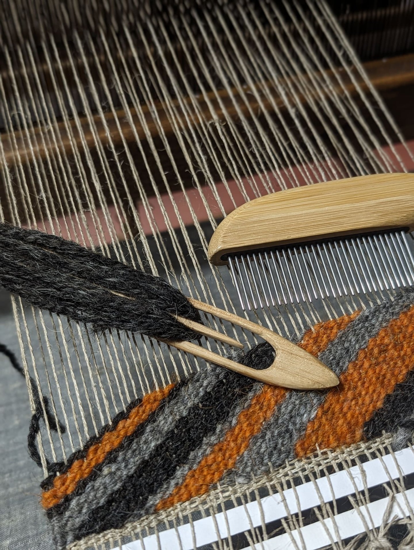 a weaving loom with shuttle, combe and black grey orange wool diagonal threads on a navajo rug in pr