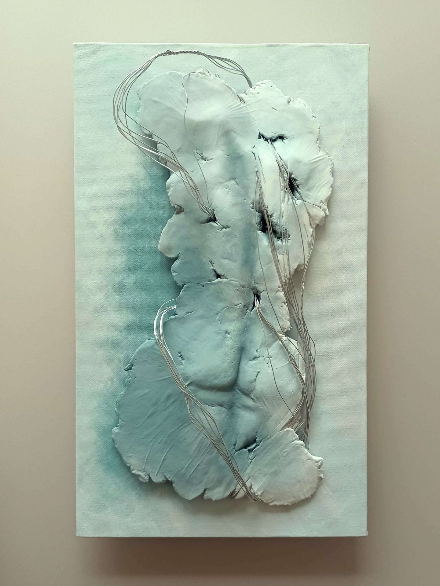 A relief sculpture of a fragmented female (rear view) entwined with wires, painted grey-blues