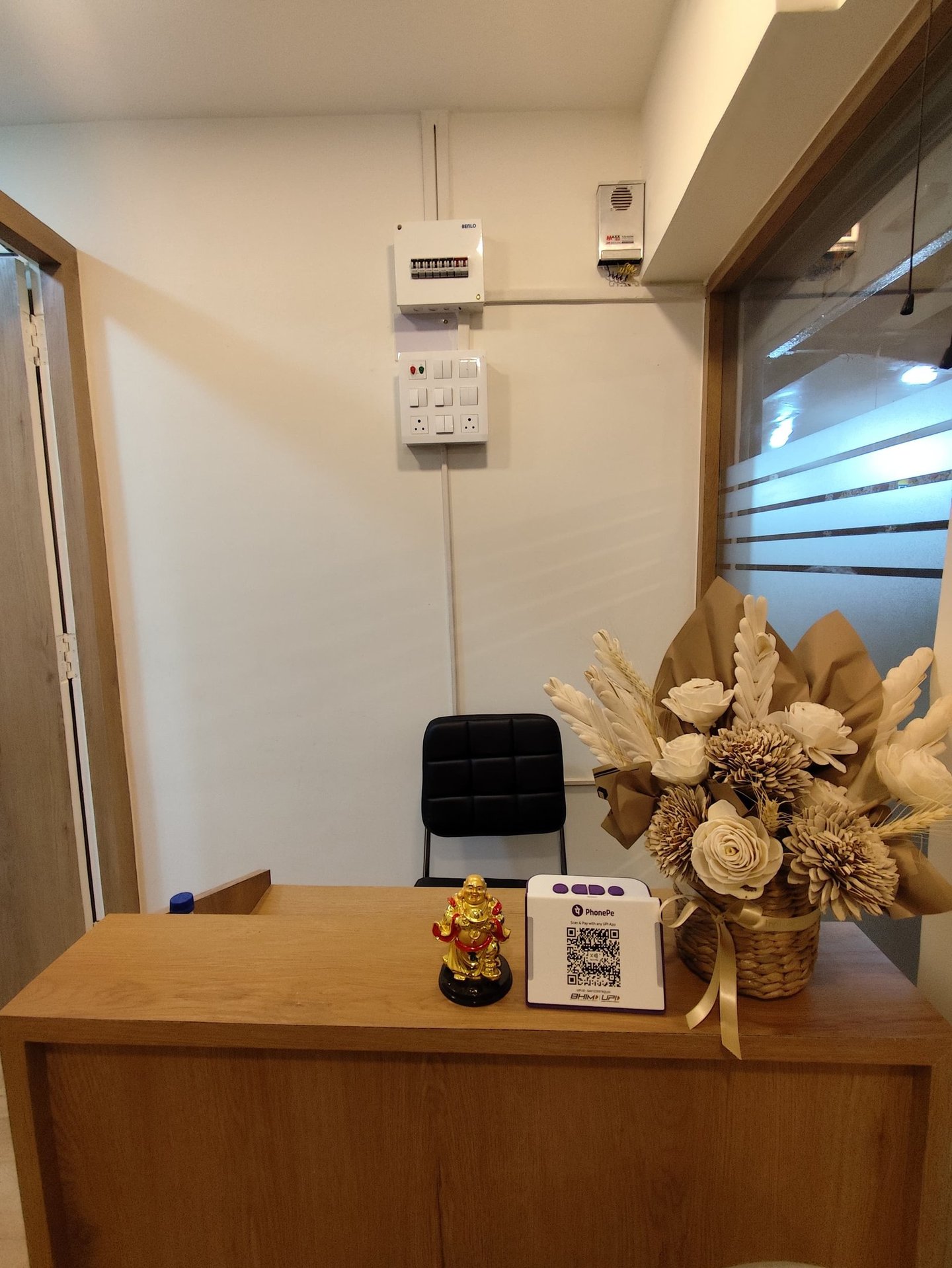 Office reception desk with flower arrangement, Buddha statue, and PhonePe QR code payment scanner.