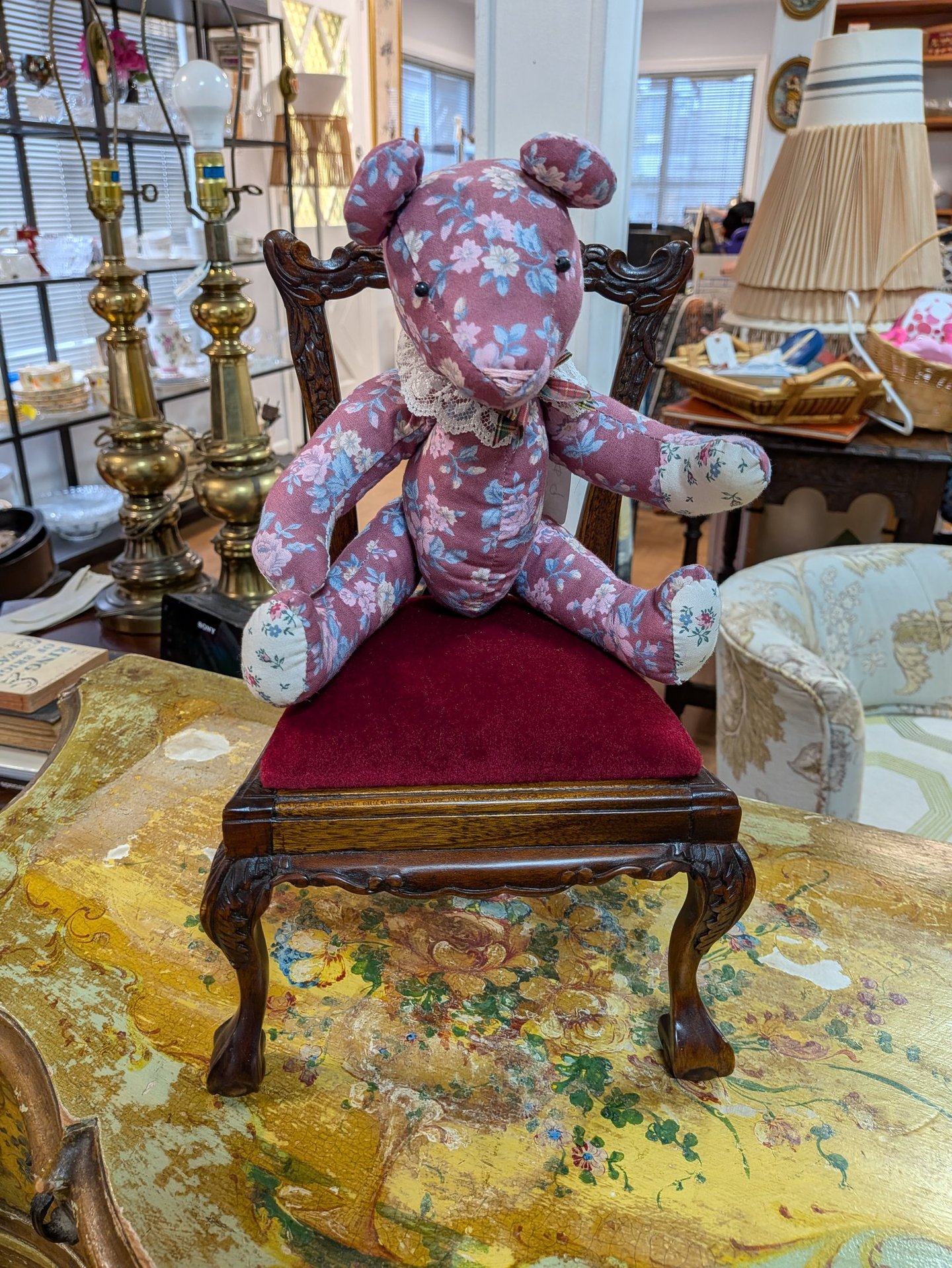 Vintage floral fabric teddy bear sitting on a miniature red velvet ornate wooden chair.