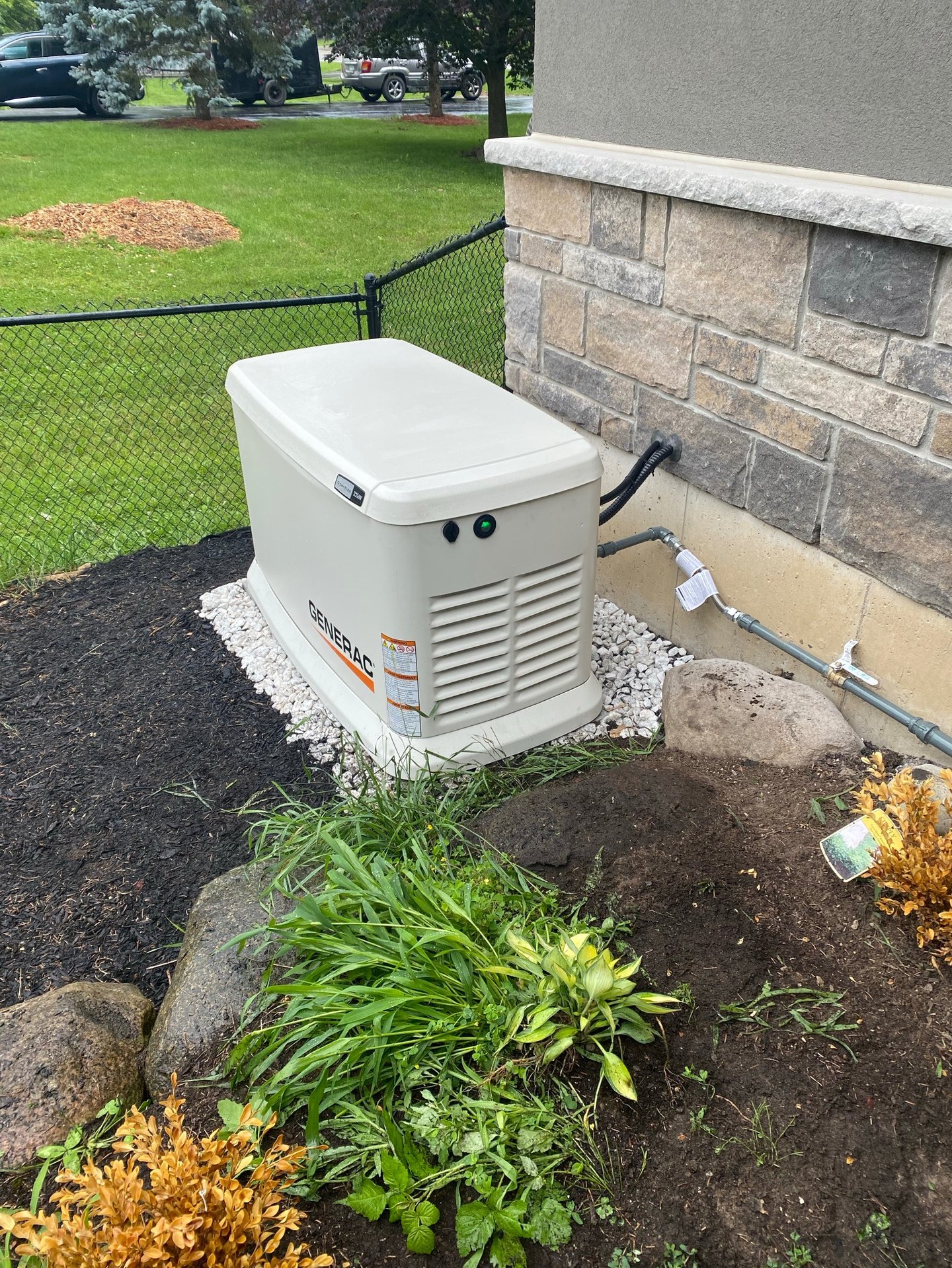 A tan Generac home standby generator installed on a gravel base next to a stone house foundation.
