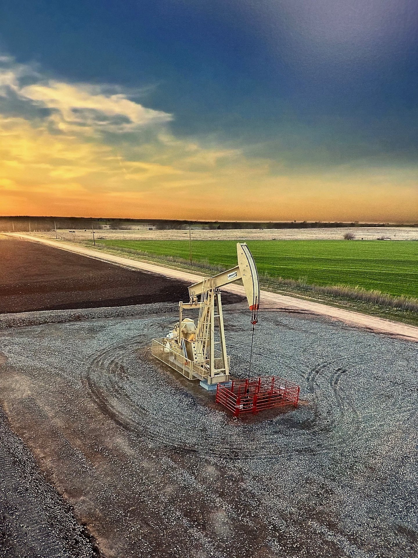 An oil pump jack operates in a rural field during a golden sunset, representing energy production.