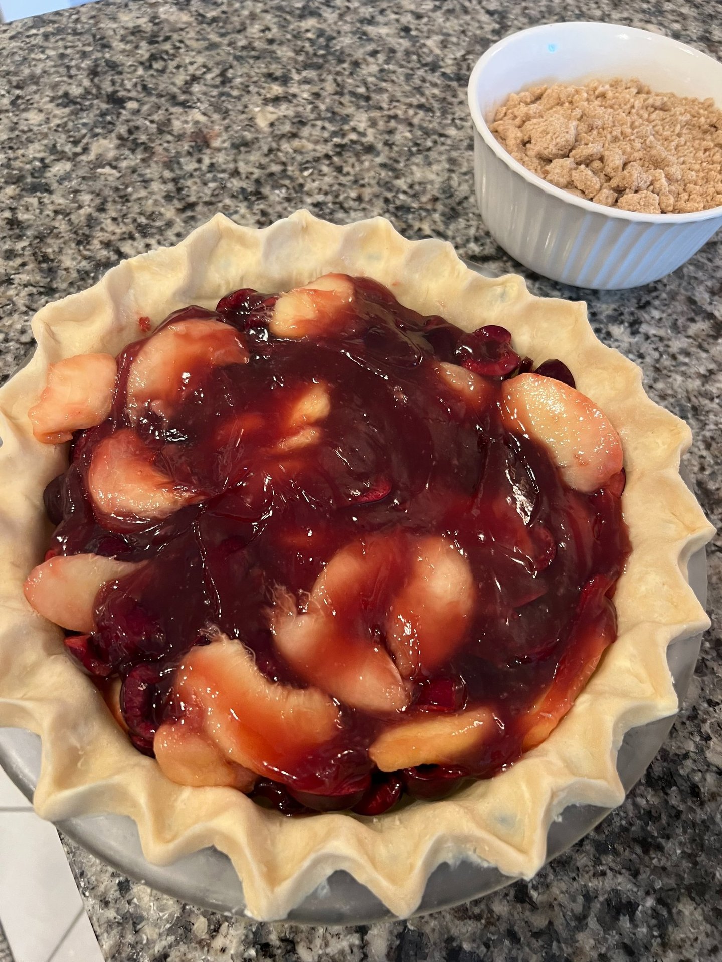 Homemade apple and cherry fruit pie filling in a fluted crust with crumble topping on the side.