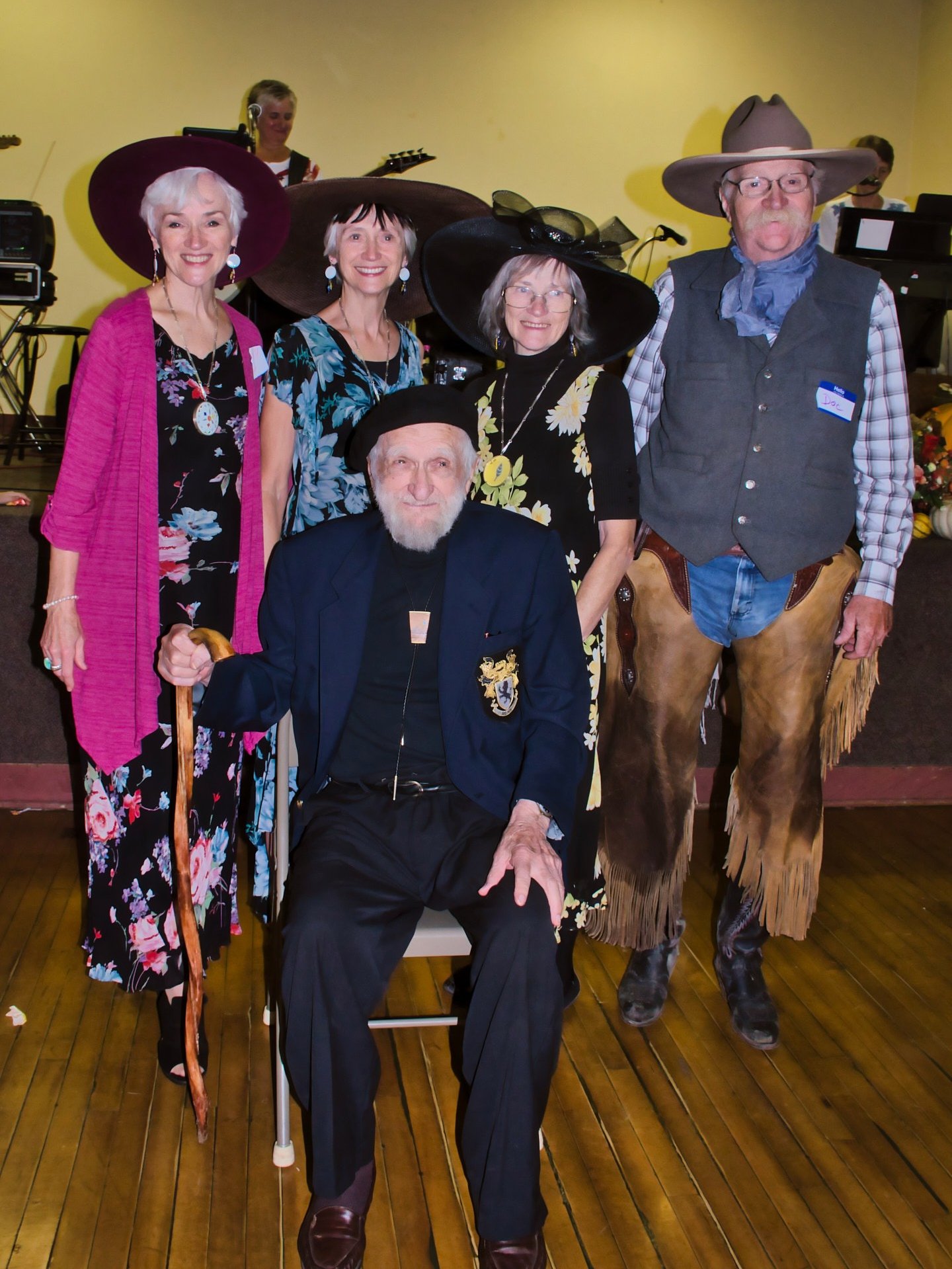four people wearing hats standing behind an old man for family group picture