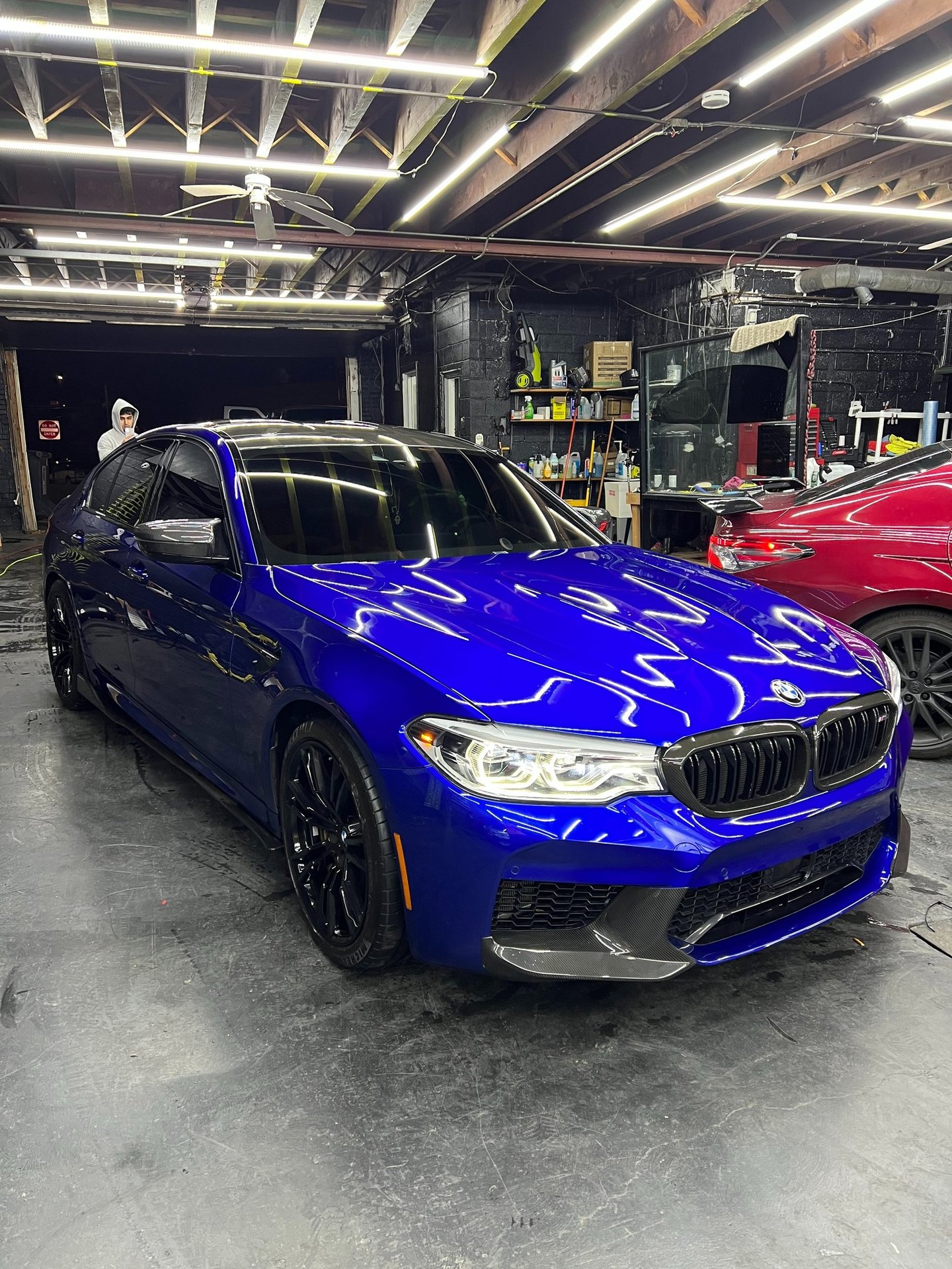 Polished blue BMW M5 sports sedan with black wheels inside a professional auto detailing shop.