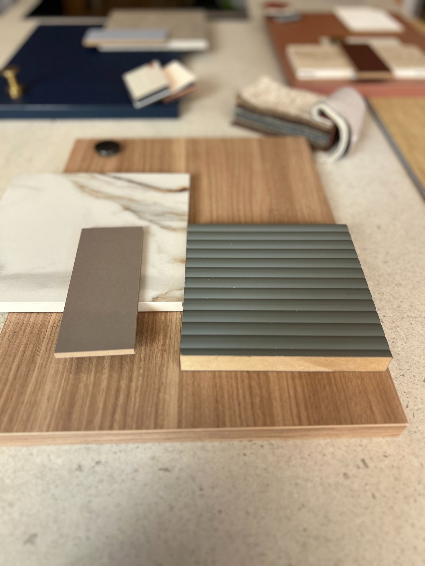 Interior design mood board featuring wood grain samples, marble tile, and fluted grey cabinetry panels.