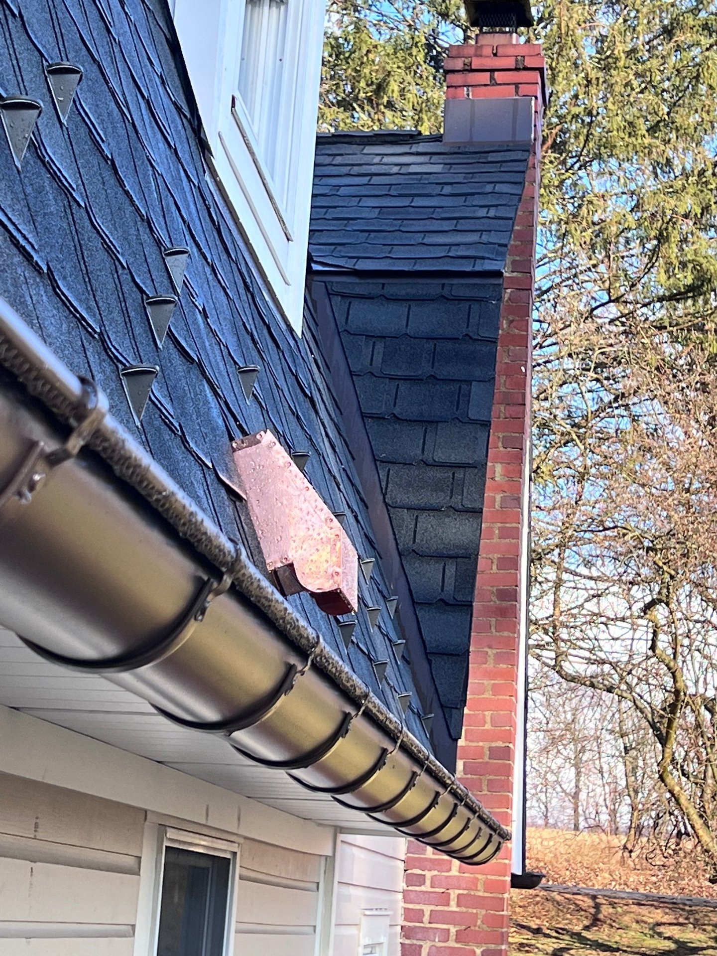 Copper flashing and snow guards installed on a steep slate shingle roof with gutters.
