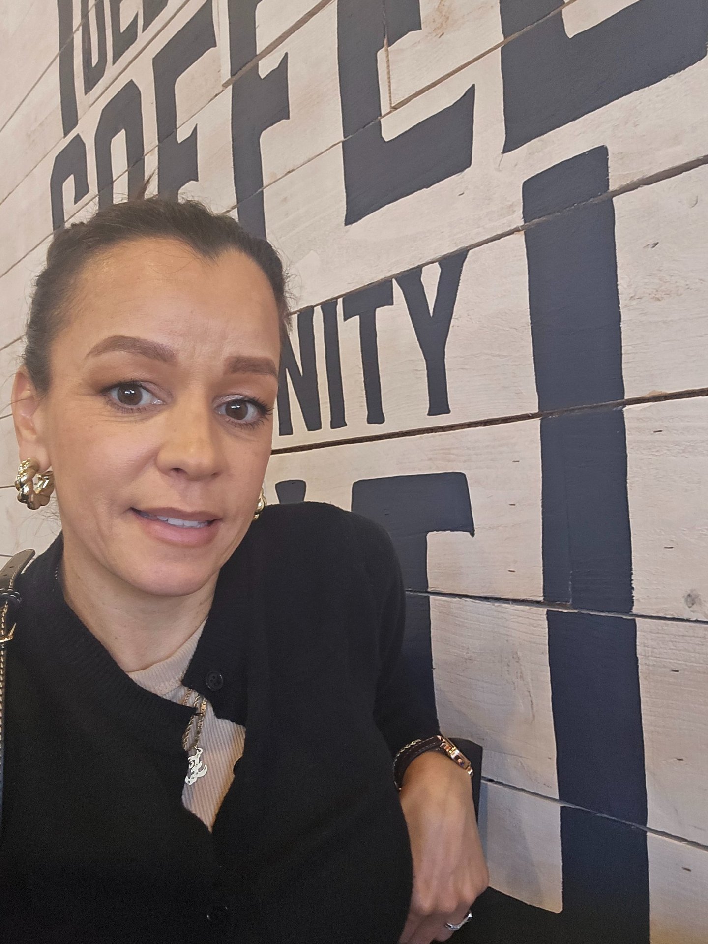 Close-up lifestyle selfie inside a coffee shop with bold wall typography in the background