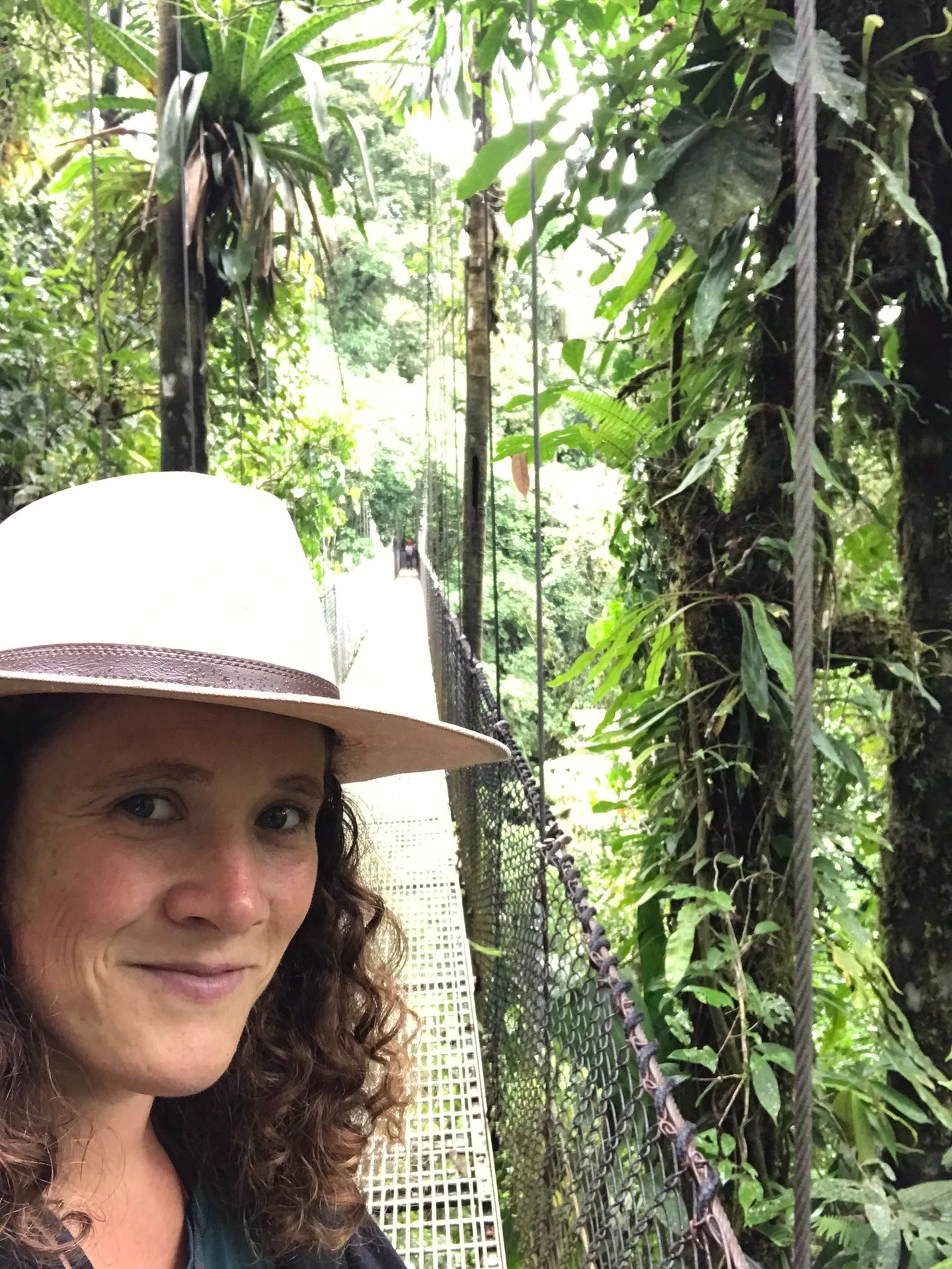 une femme aux cheveux frisés sur un pont suspendu au costa rica, un léger sourire sur les lèvres