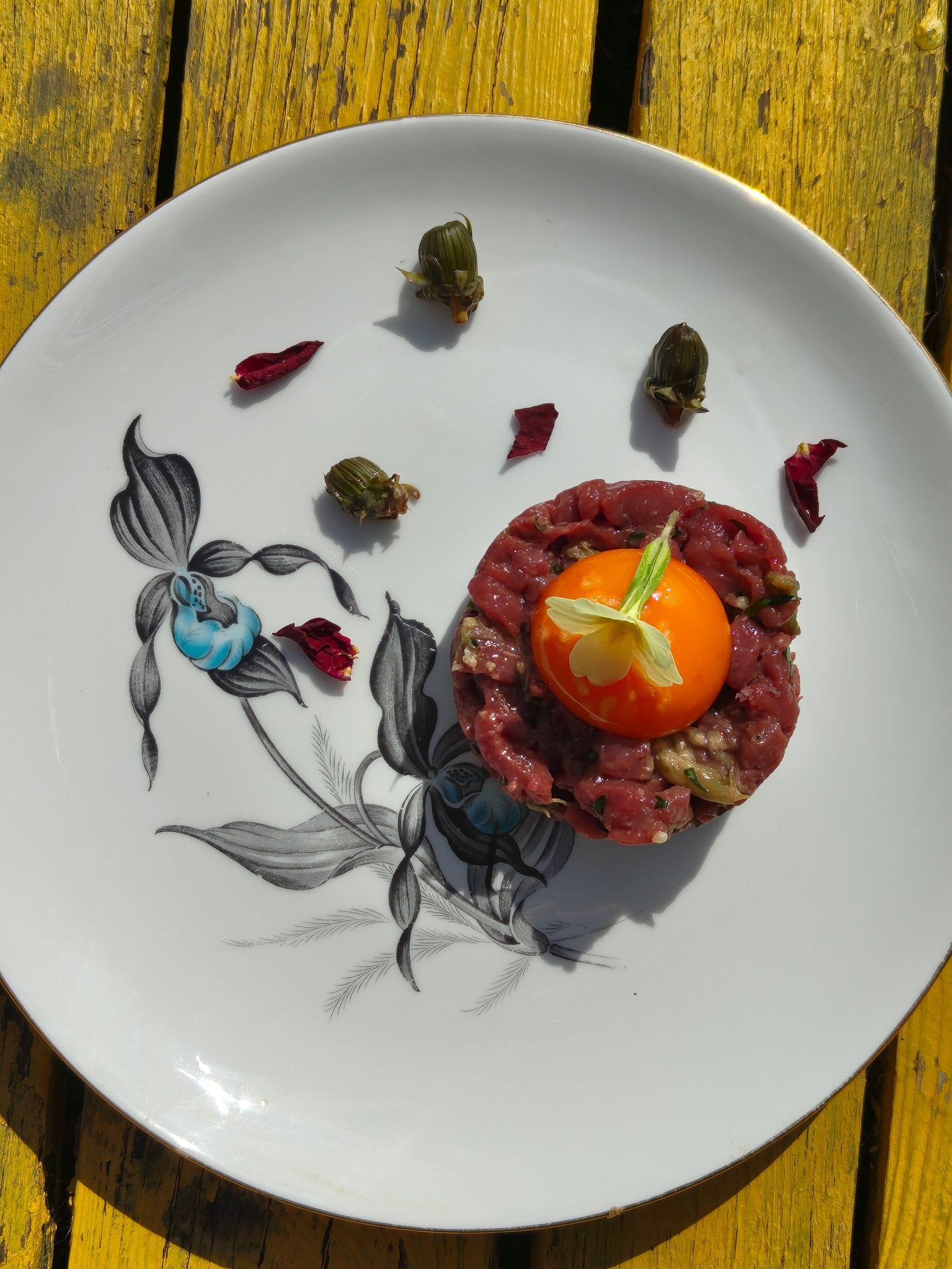 Venison tartar with an egg yolk, primrose garnish, dandelion capers and rose petals