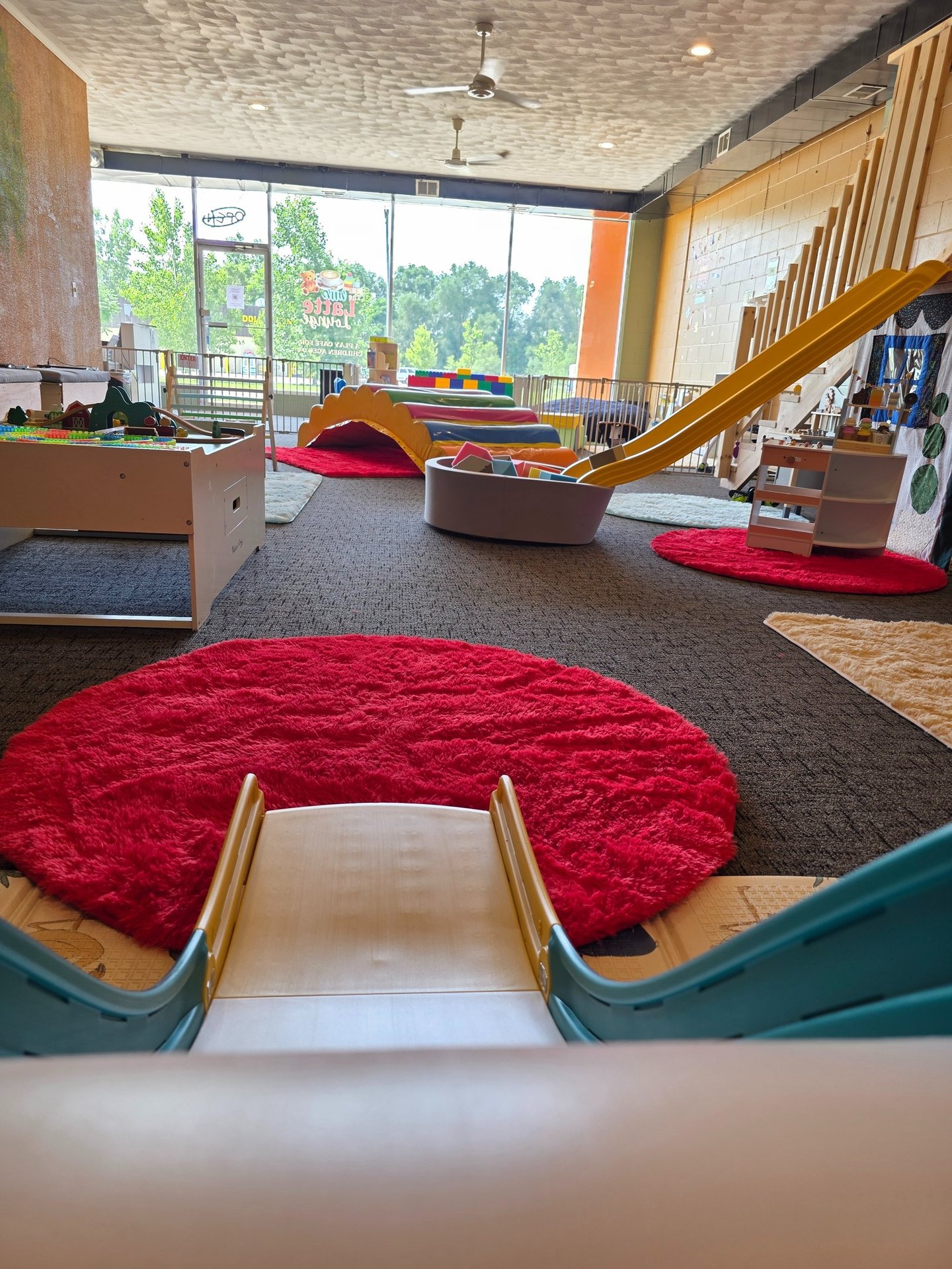 Indoor playground for toddlers featuring colorful slides, soft play mats, a train table, and more.