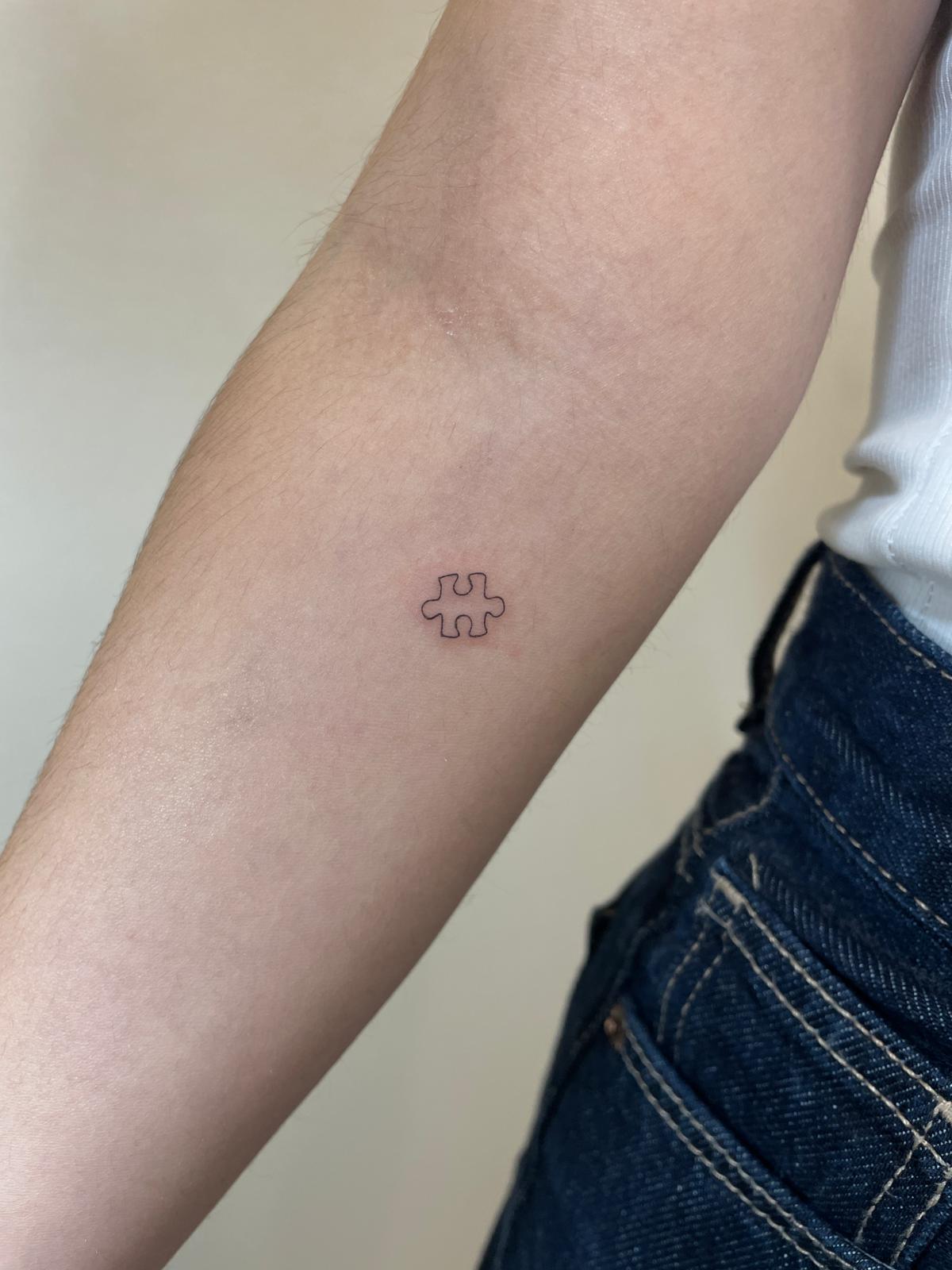 Tatuaje fineline en Madrid de pieza de puzzle en trazo fino y minimalista en el antebrazo