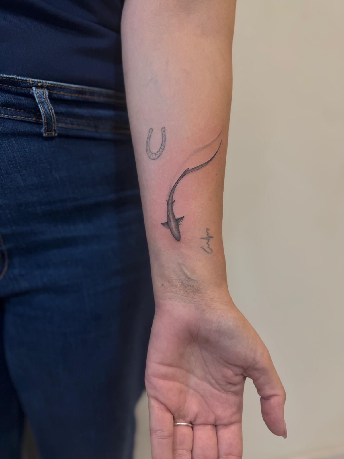 Tatuaje fineline en Madrid de tiburón realista en movimiento con herradura y nombre en cursiva