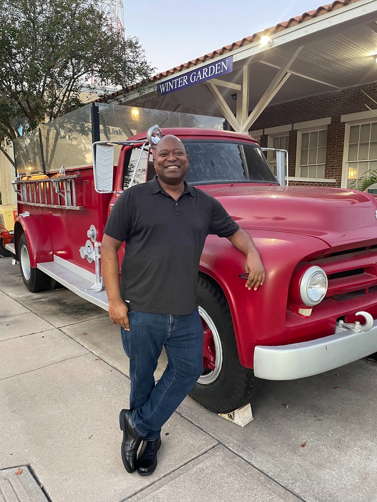 Photo of attractive dark skinned male leaning against a vintage red fire truck