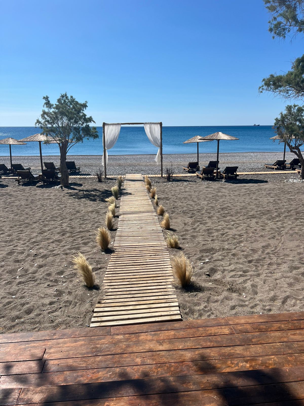 Wooden walkway leading to a beachfront wedding arch with sunbeds and umbrellas on a sandy beach.