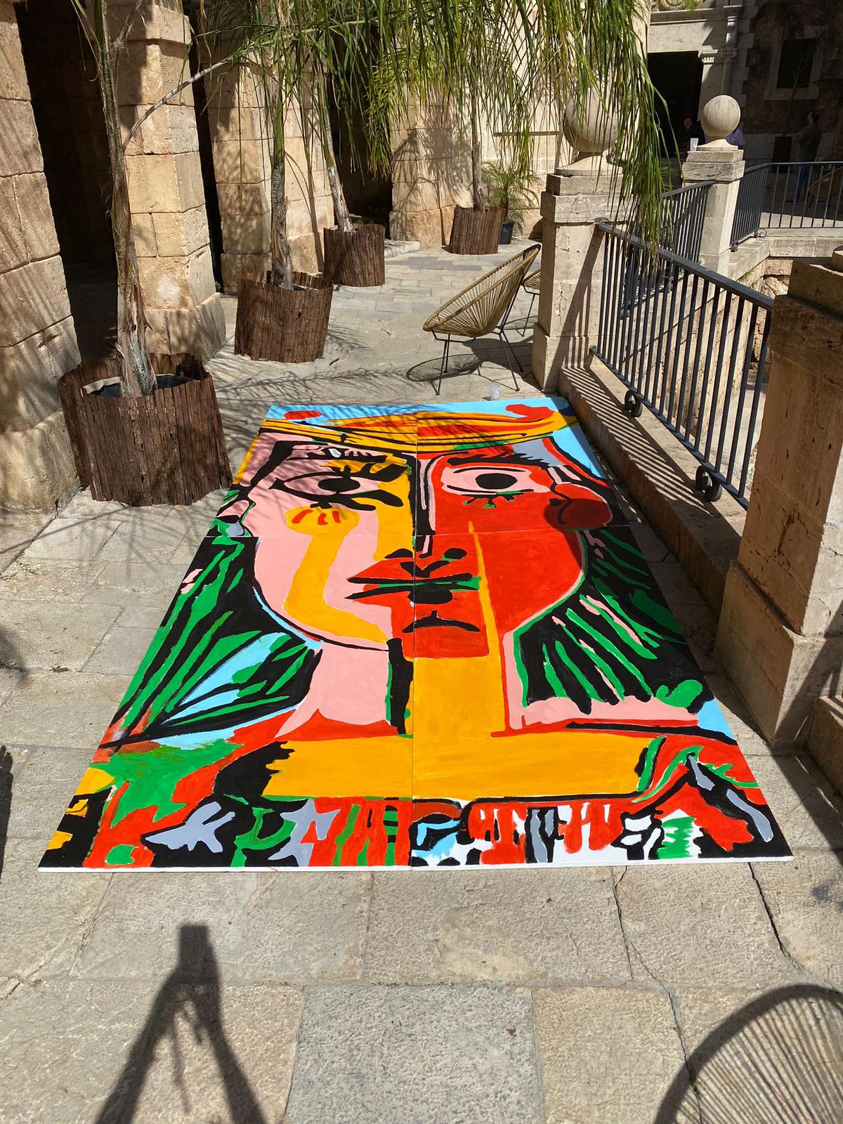A vibrant cubist abstract portrait painting displayed on a stone patio in an outdoor courtyard.