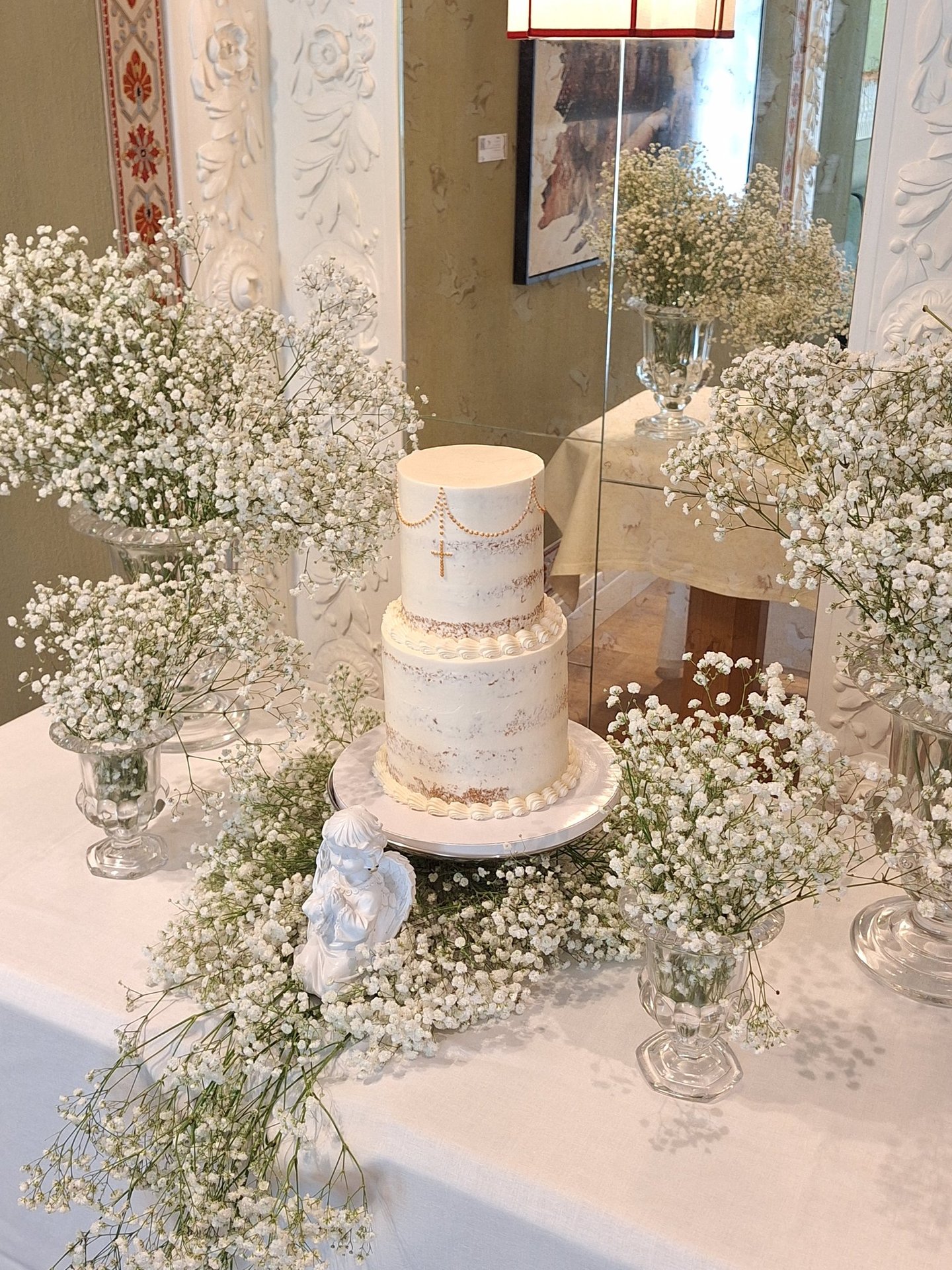 Elegant two-tier white baptism cake with gold cross and baby's breath floral arrangements.