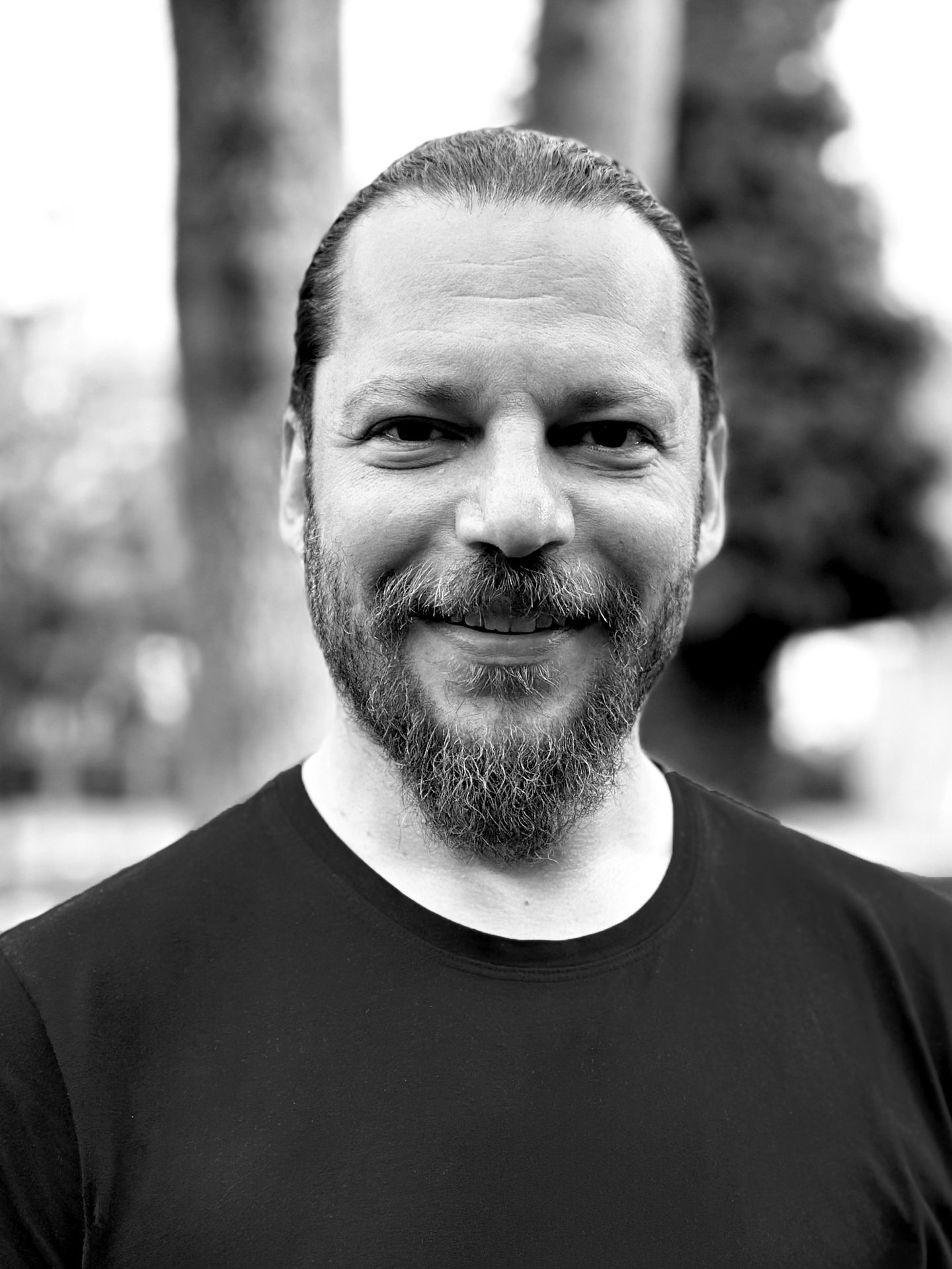 Alper Sümengen Tai Ji Qi Gong and sword instructor of WDP Turkey, smiling outdoors in black shirt