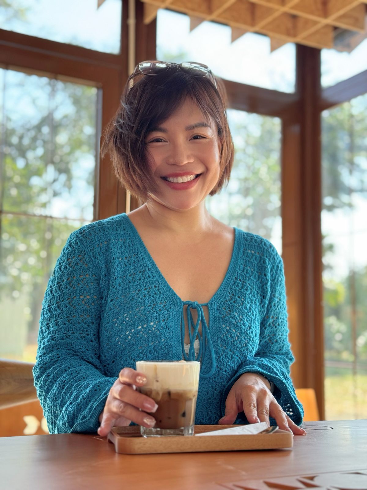 Tina in a blue sweater is smiling and holding a coffee