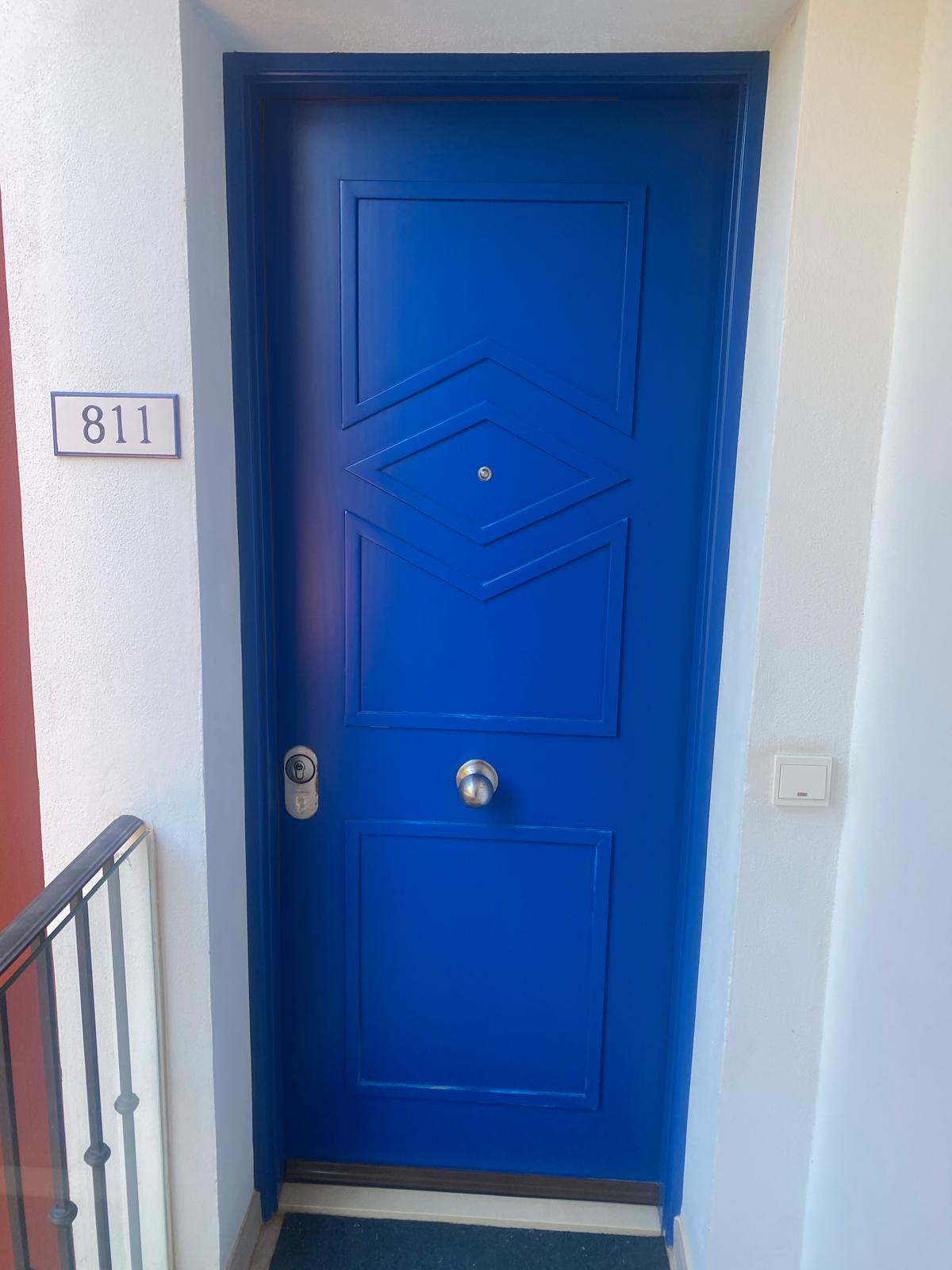 A vibrant blue modern front door with a silver knob and number 811 sign on white exterior wall.