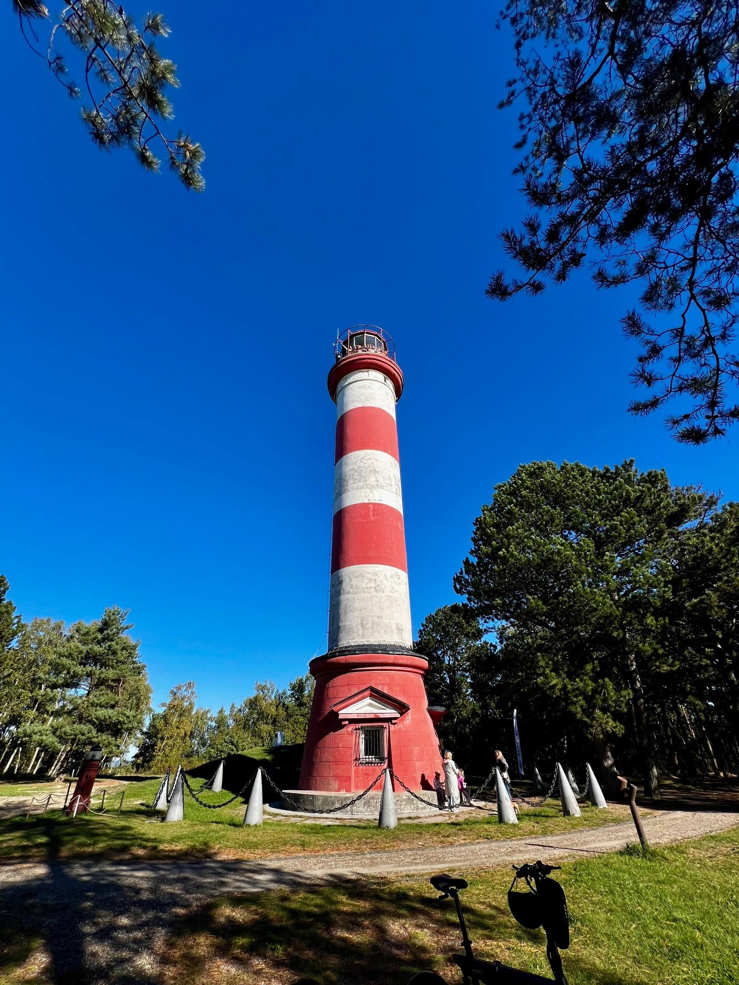 Historic Nida lighthouse tower standing tall under a clear blue sky surrounded by green trees.