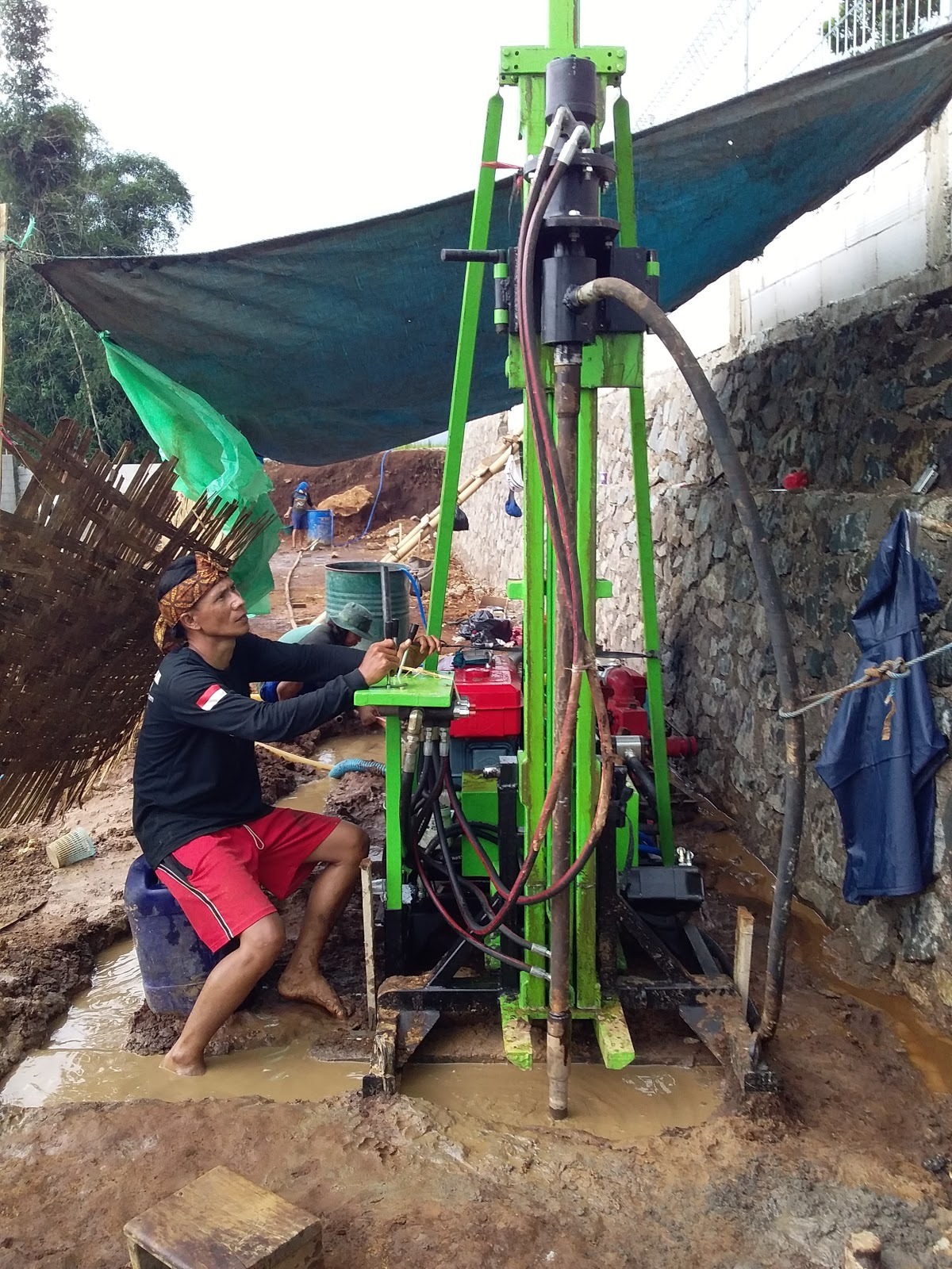 Technician operating a portable hydraulic water well drilling rig at an outdoor construction site.