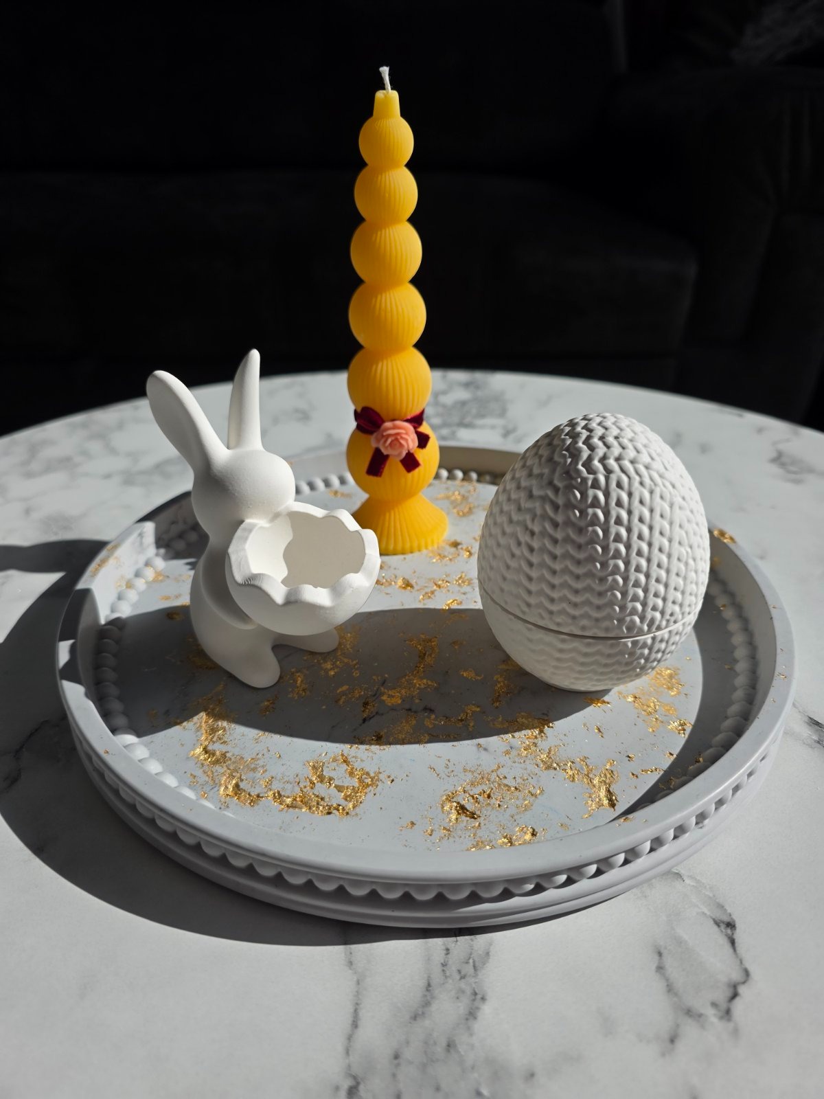 Minimalist Easter decor featuring a white bunny holder, textured egg, and yellow candle on a marble tray.