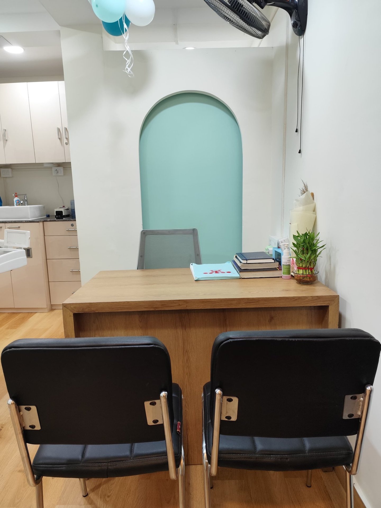 A modern medical office consultation desk with black guest chairs and a teal arched wall accent.