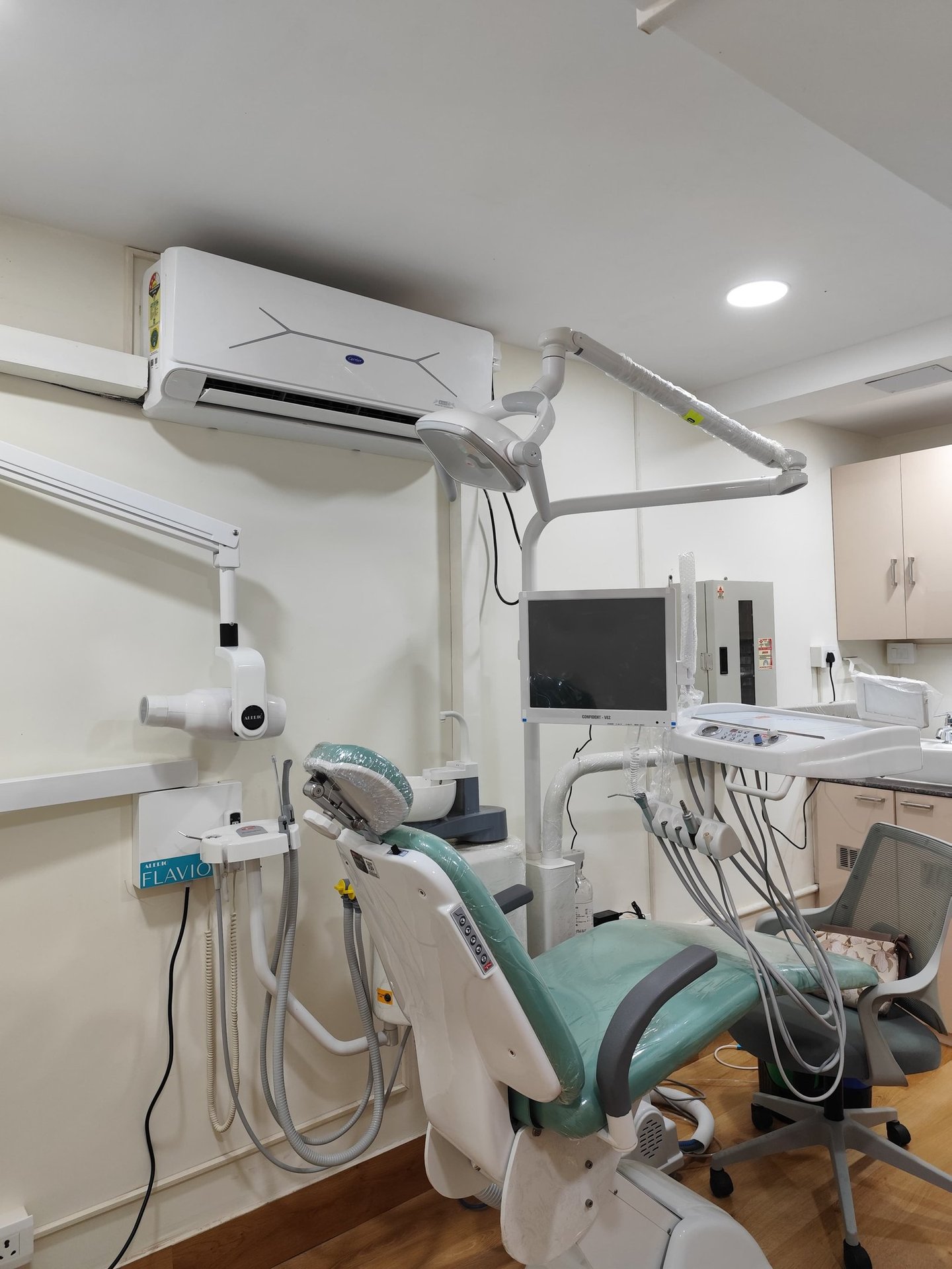 Modern dental clinic room with an adjustable green examination chair and medical imaging equipment.