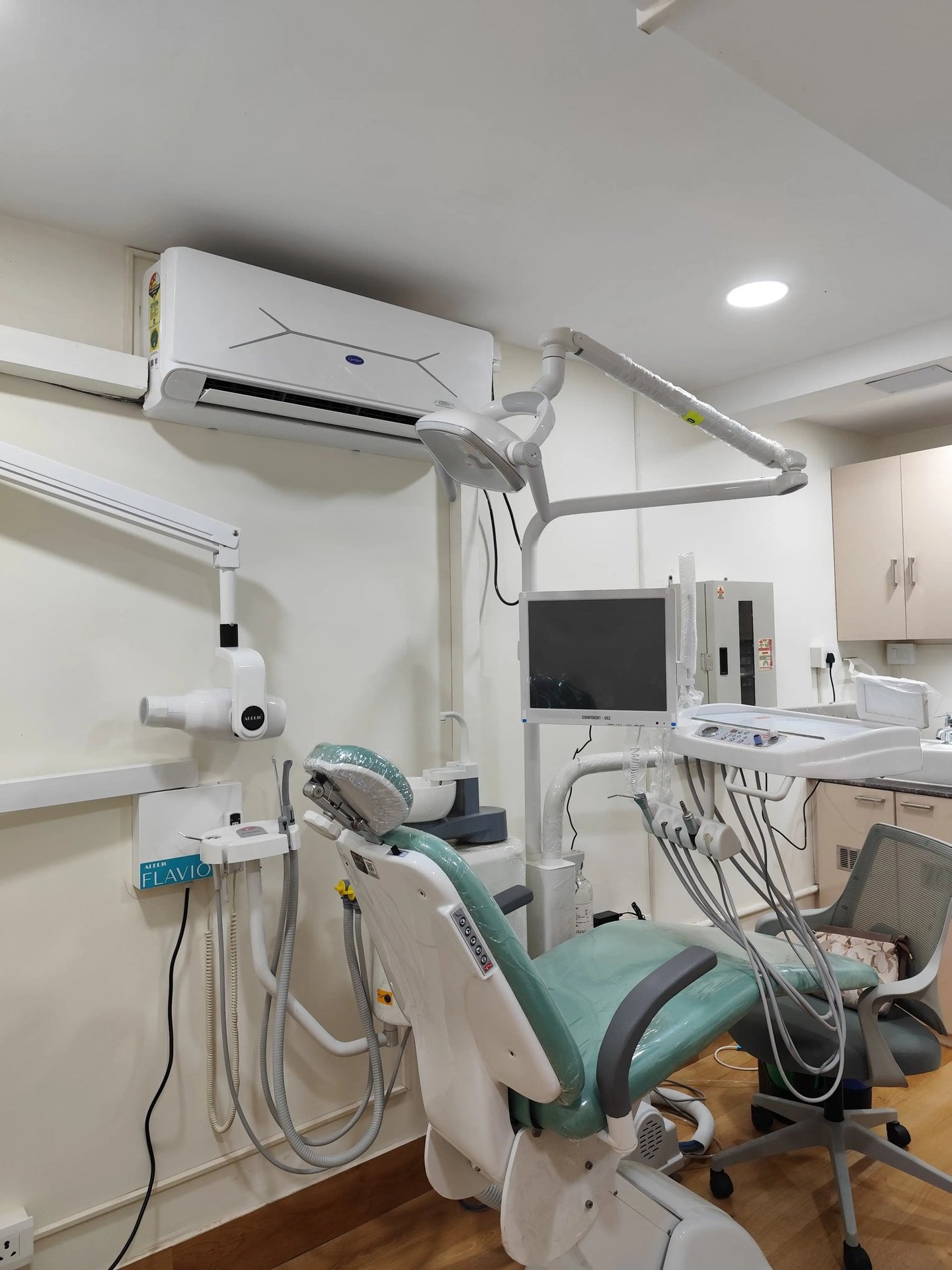 Modern dental clinic room with an adjustable green examination chair and medical imaging equipment.