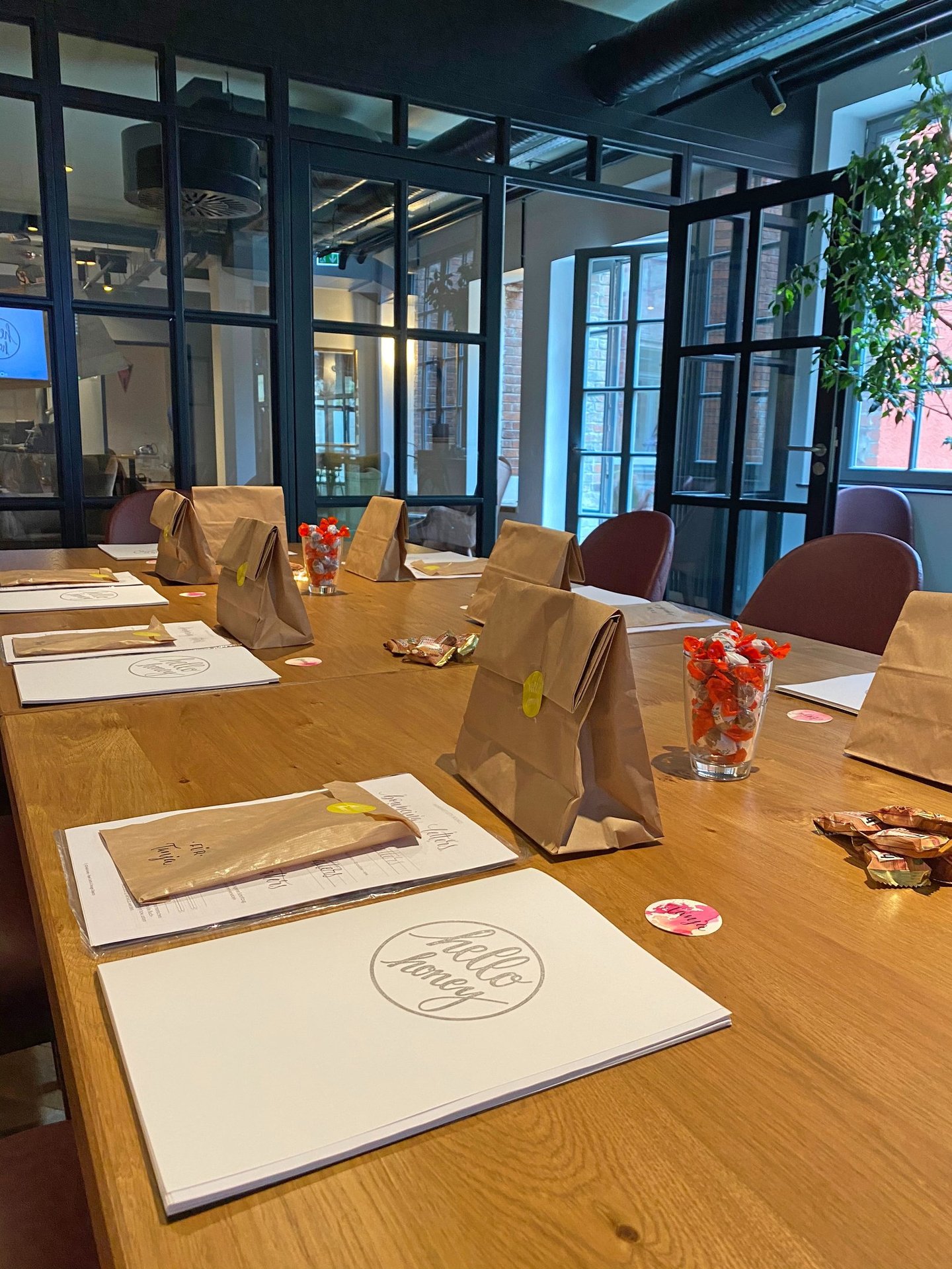 Brown paper gift bags and event programs on a wooden conference table in a modern office meeting room.