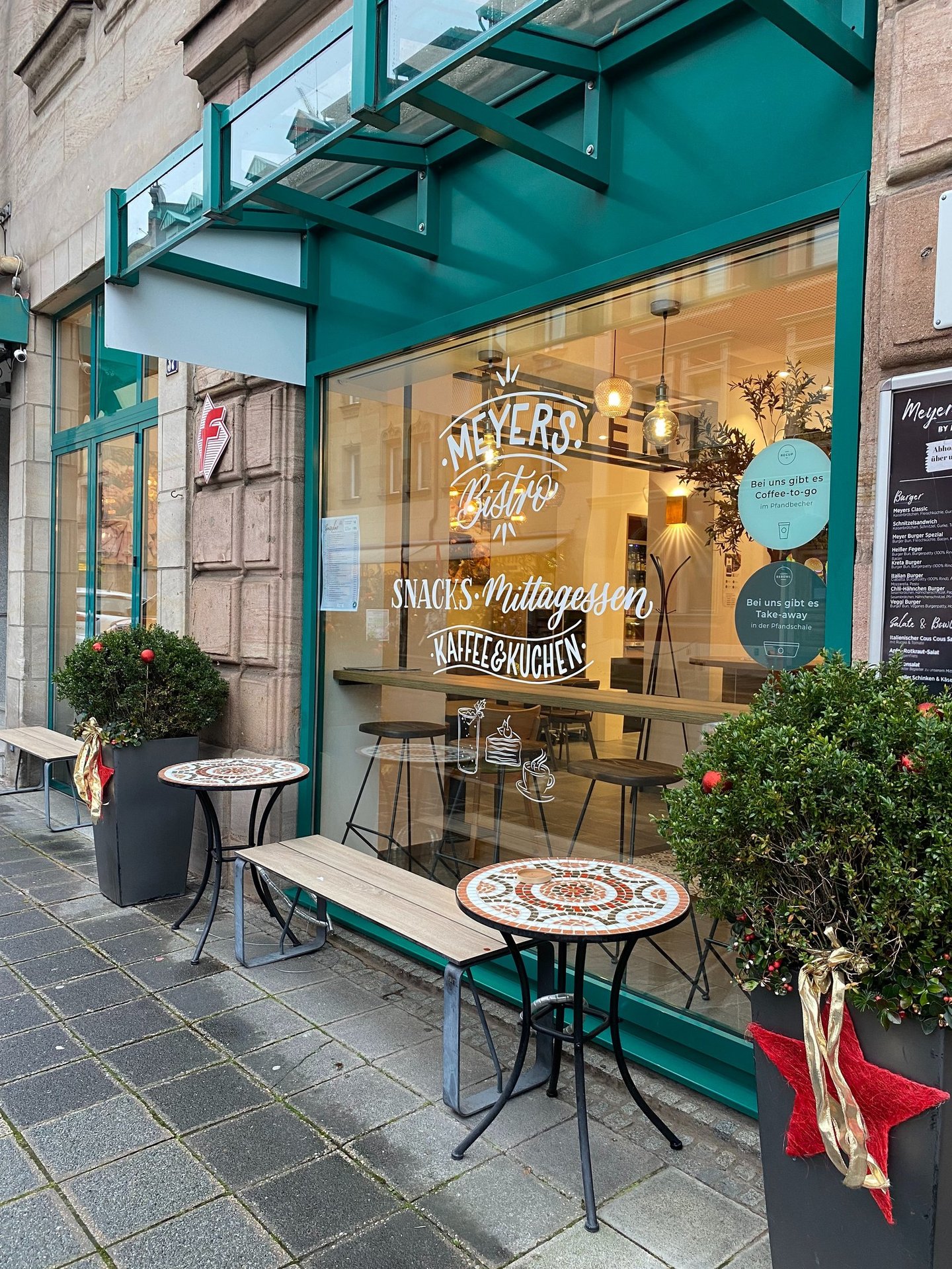 Meyers Bistro storefront with teal window frames, outdoor mosaic tables, and holiday decorations.