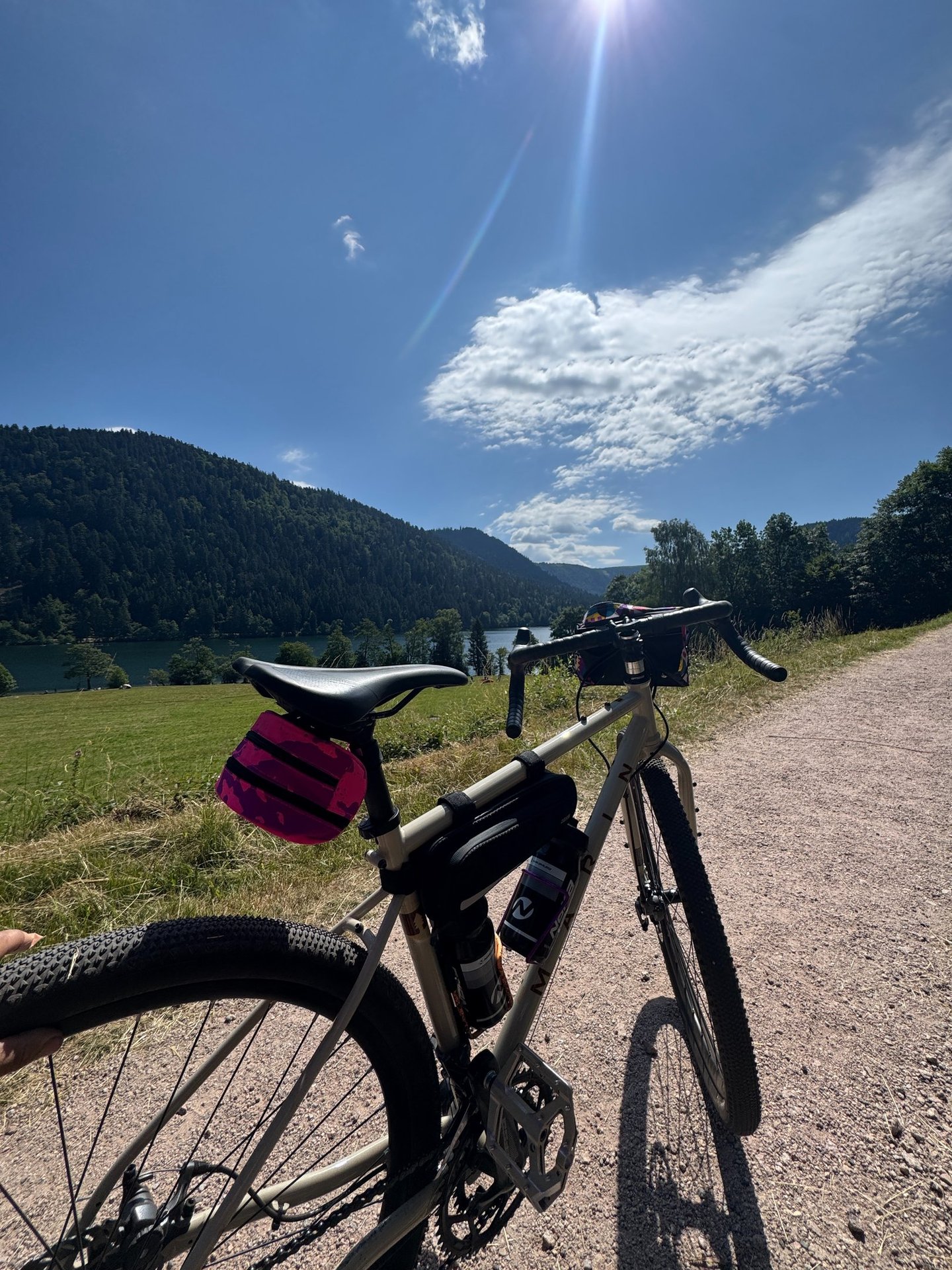 Gravel bike with bikepacking bags parked on a scenic trail overlooking a lake and mountains.