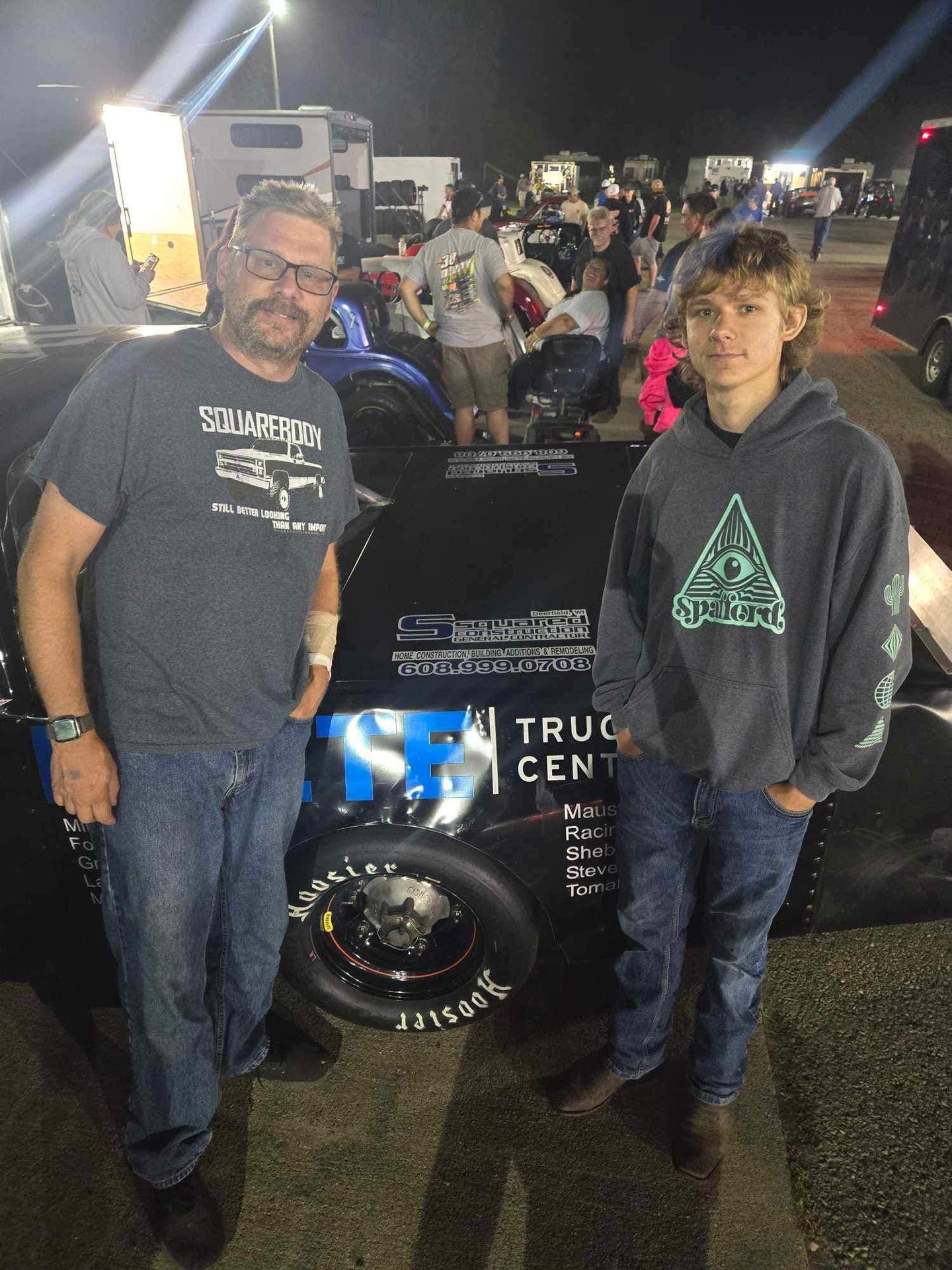 Owner and his father standing in front of a race car sponsored by S Squared Construction, featuring 