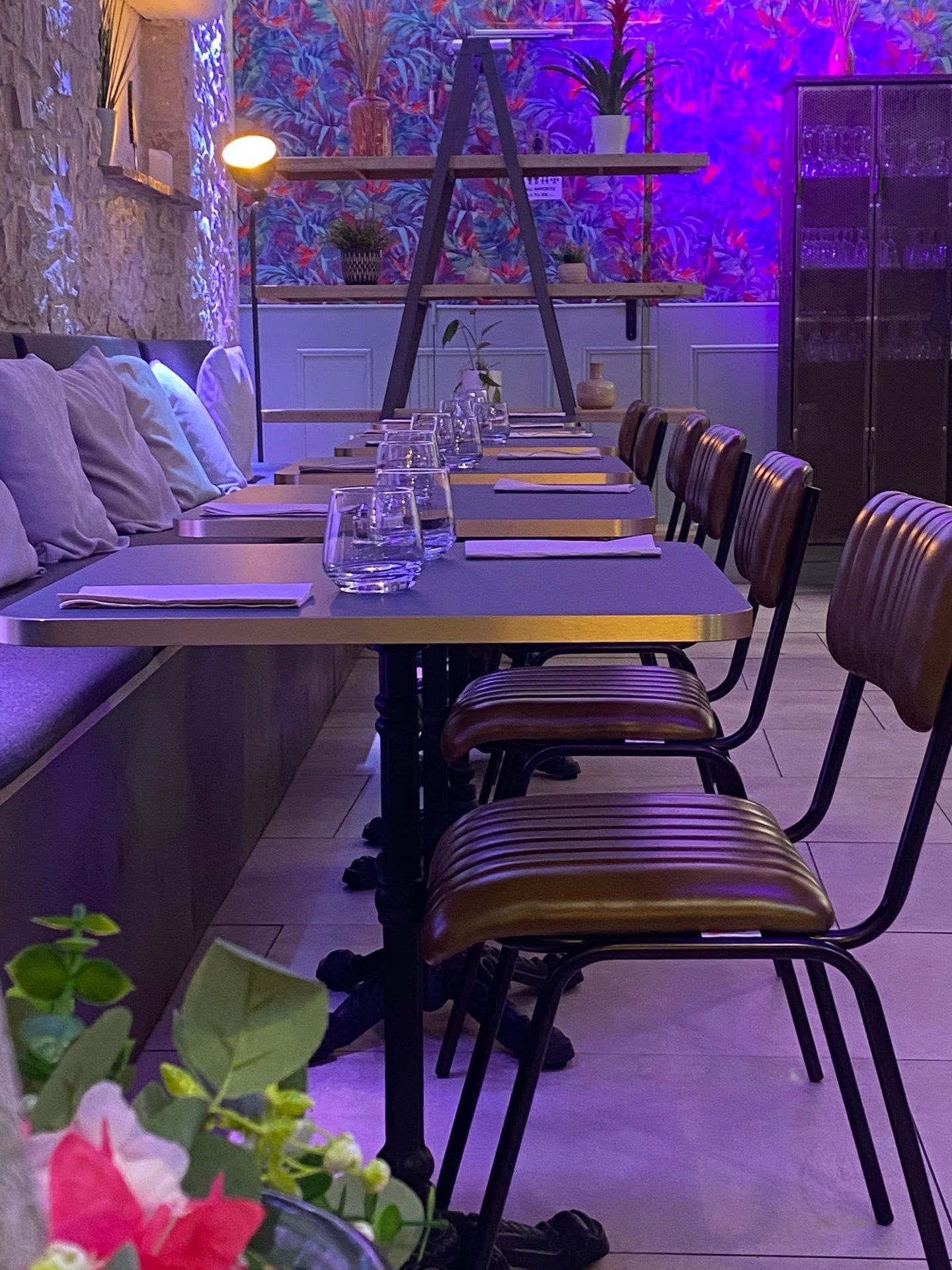 Modern restaurant dining area with leather chairs, set tables, and vibrant purple neon lighting.