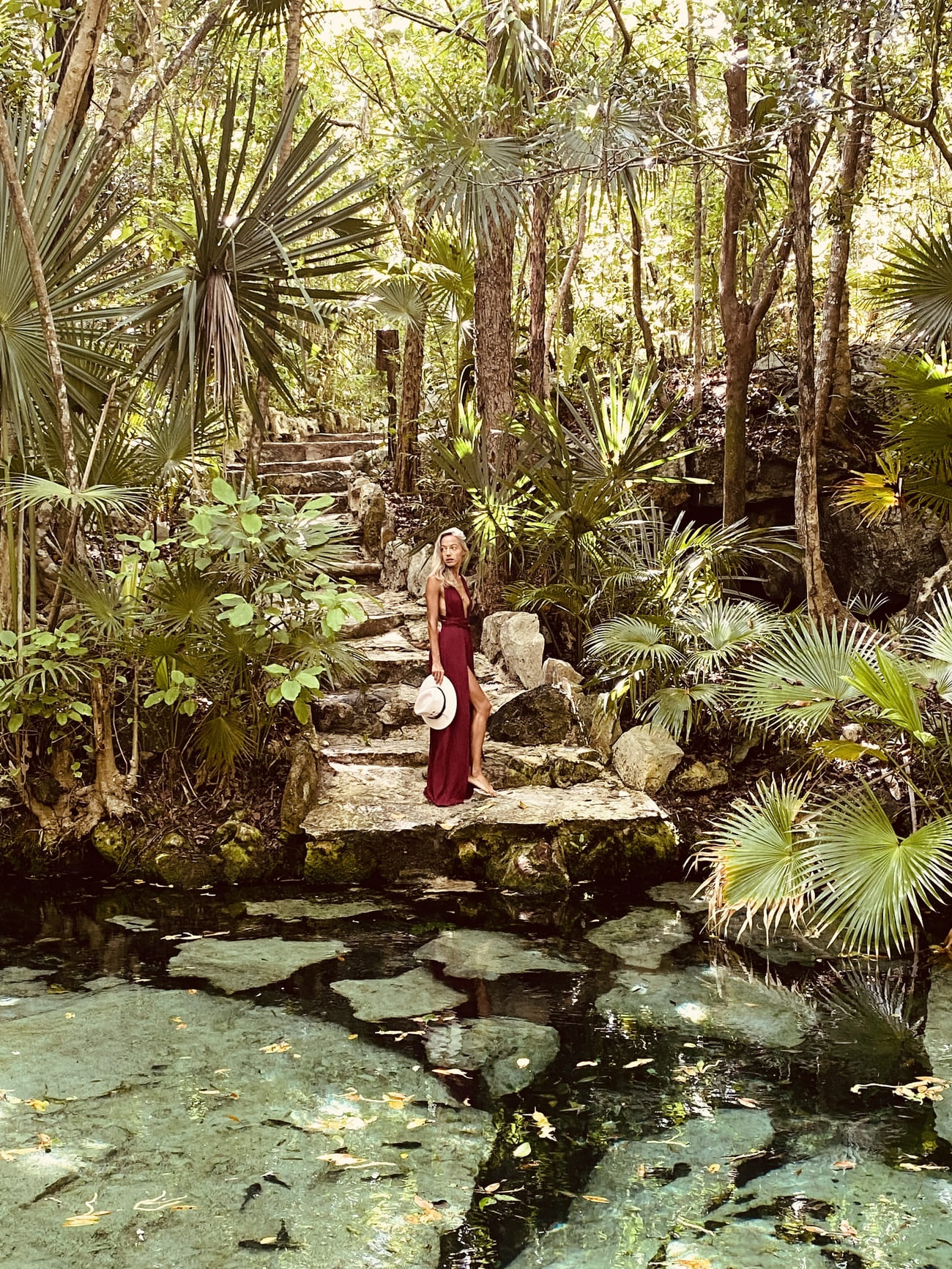 mujer en un cenote usando vestido rojo boho y sombrero en la mano. jungla selva. Tulum