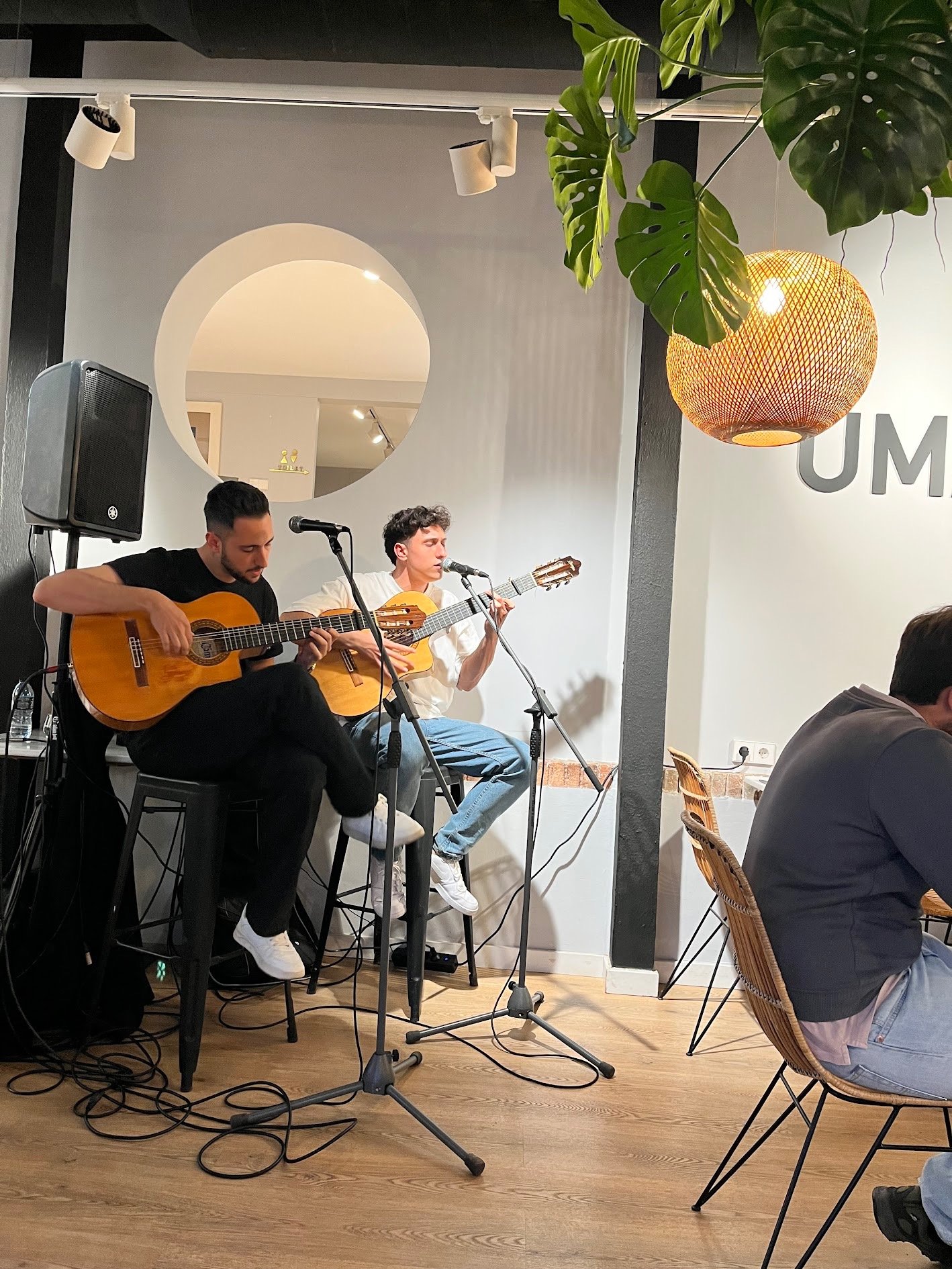 Two young musicians playing acoustic guitars and singing live at a cozy cafe with modern decor.