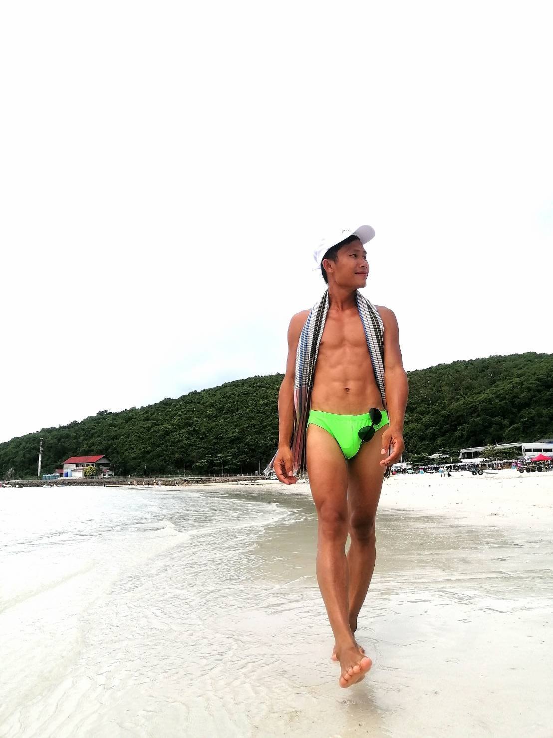 Man walking along Pattaya Beach wearing green swimming trunks.