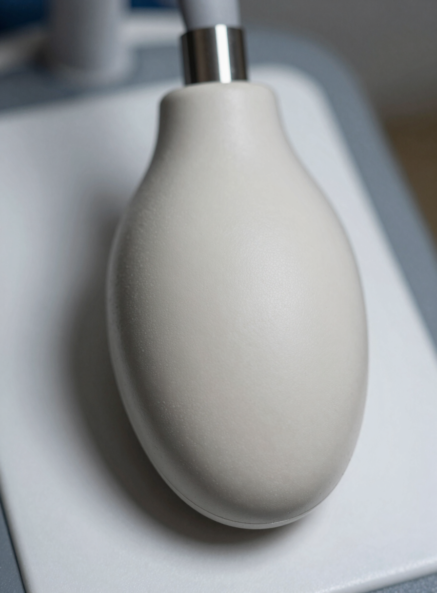 Extreme close-up of a convex ultrasound probe head resting on a white clinical surface, curved transducer face filling the lower frame, clinical overhead lighting, fine surface texture and cable connector visible at top, no hands, no branding