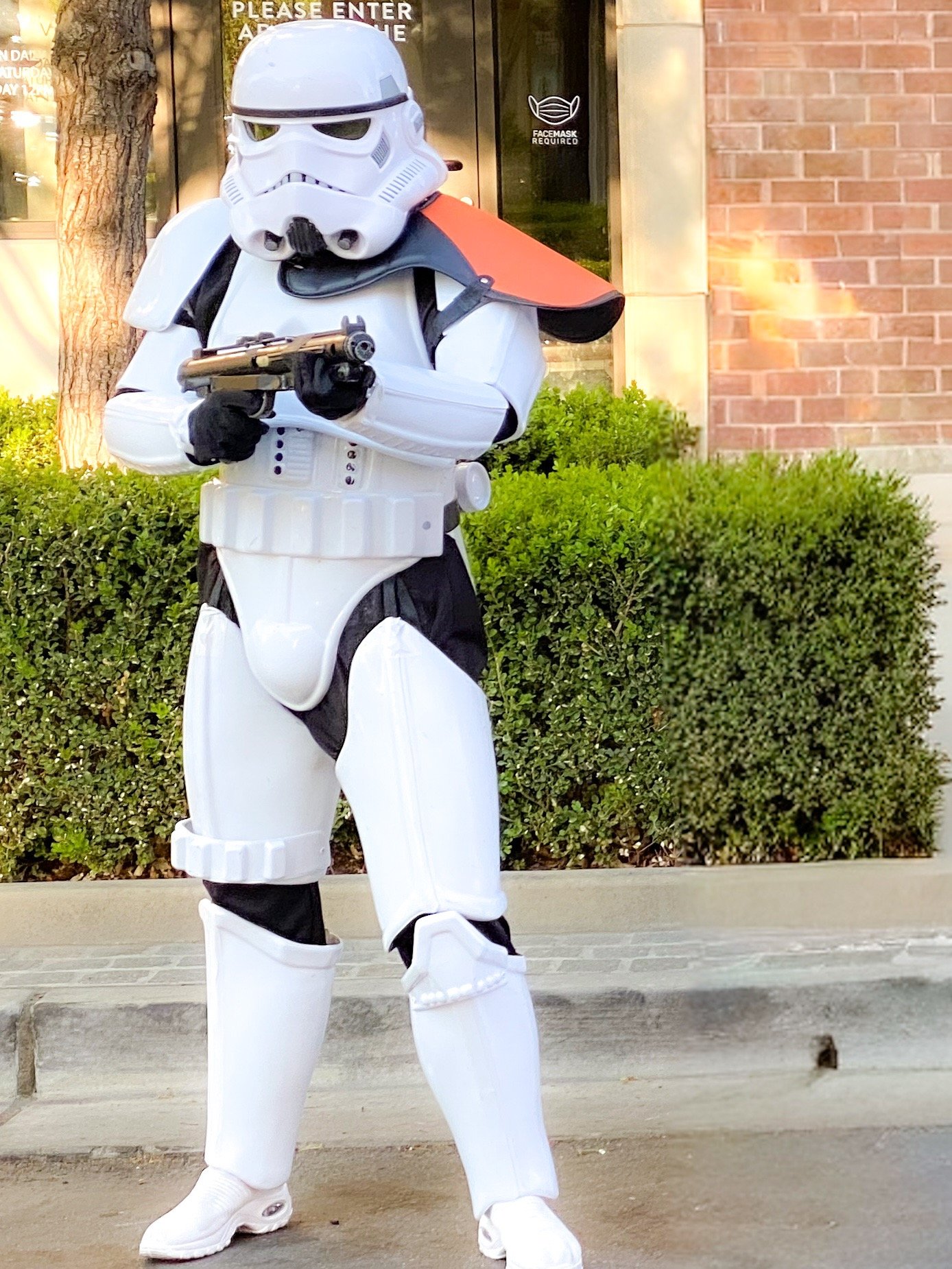 A person in a detailed Star Wars Stormtrooper cosplay costume holding a blaster rifle outdoors.
