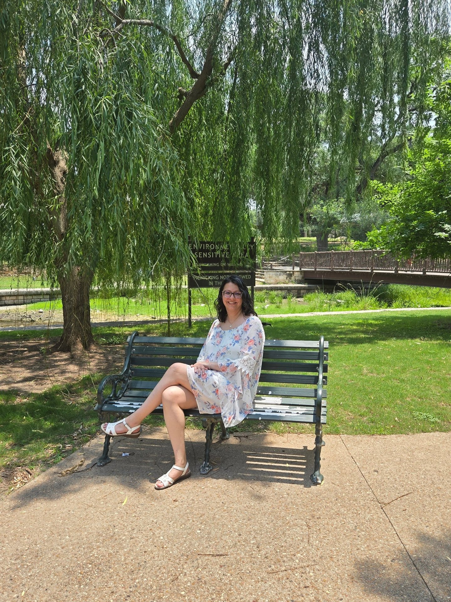 Angela sitting on a bench in the park under a tree.