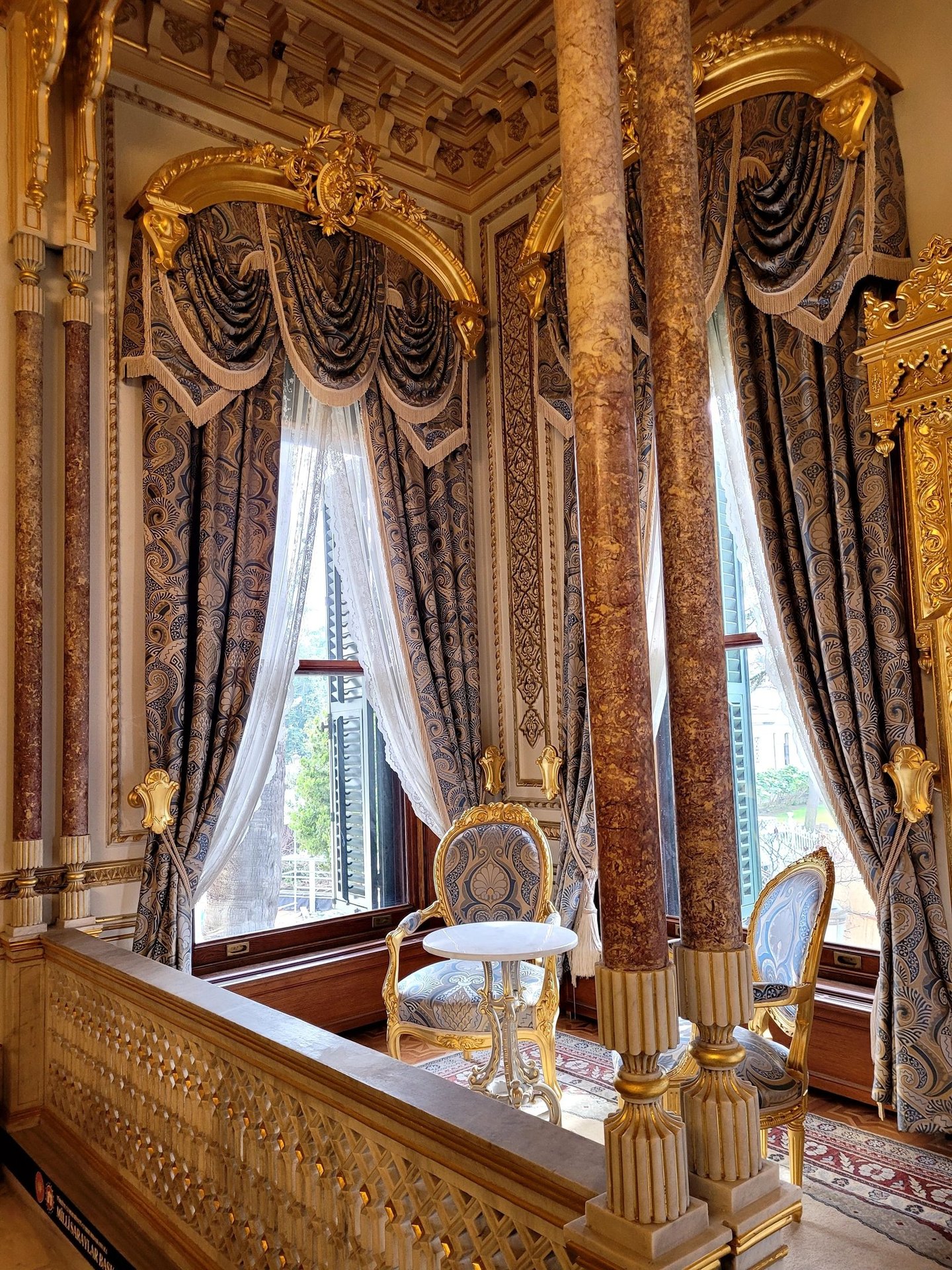 Opulent palace interior featuring marble columns, ornate gold trim, and luxurious blue damask curtains.