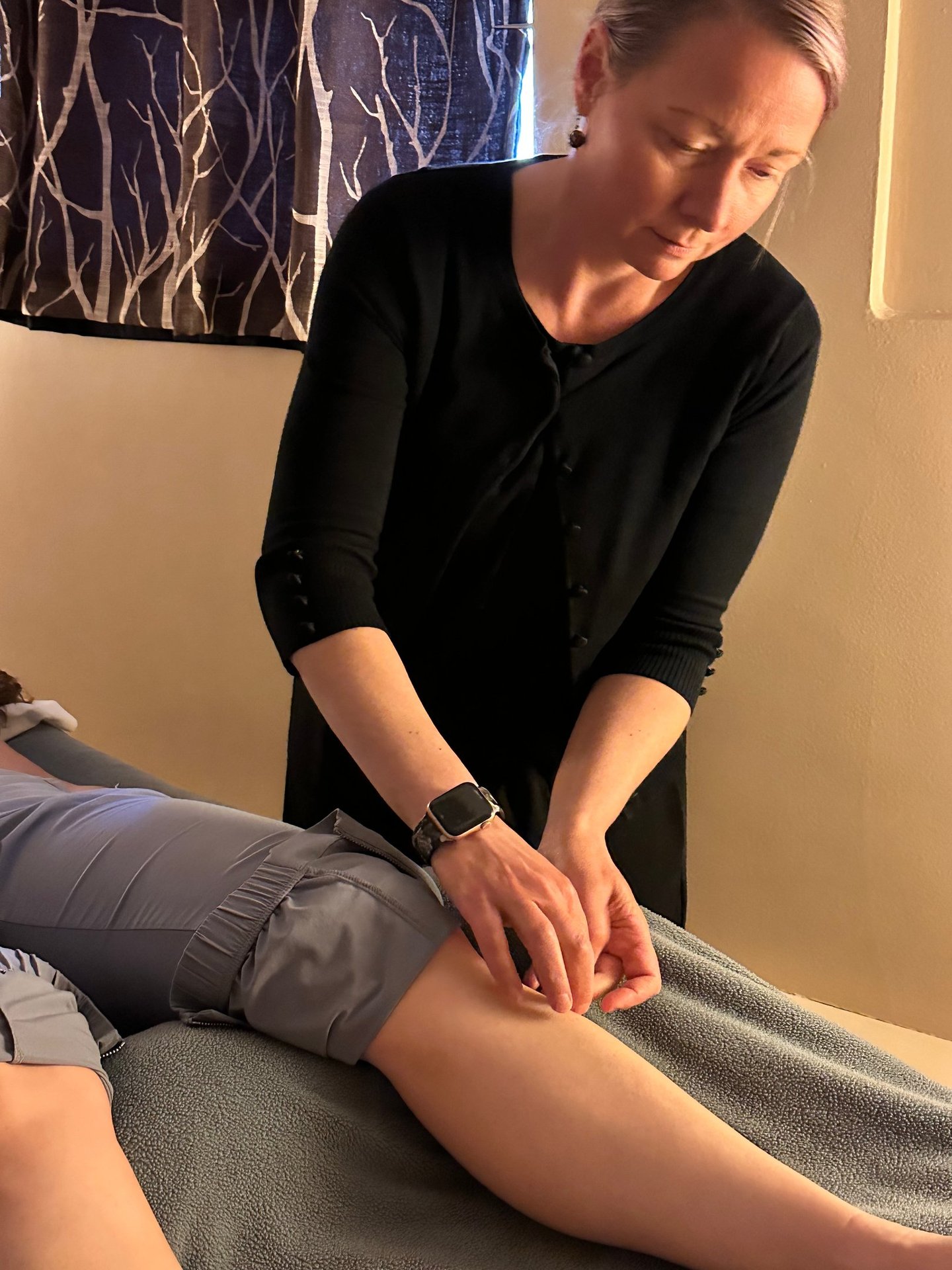 Acupuncturist inserting needle into patient’s lower leg on acupuncture table. 