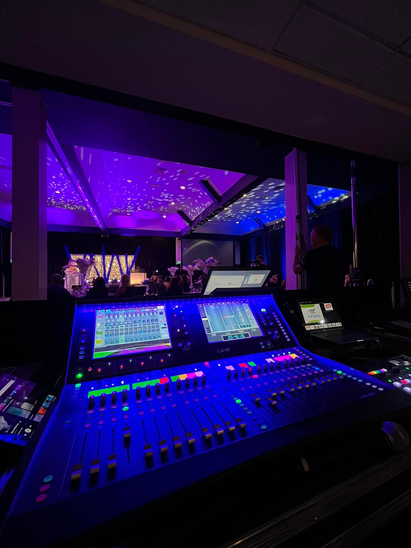 Professional digital audio mixing console with glowing blue lights at a live event venue.